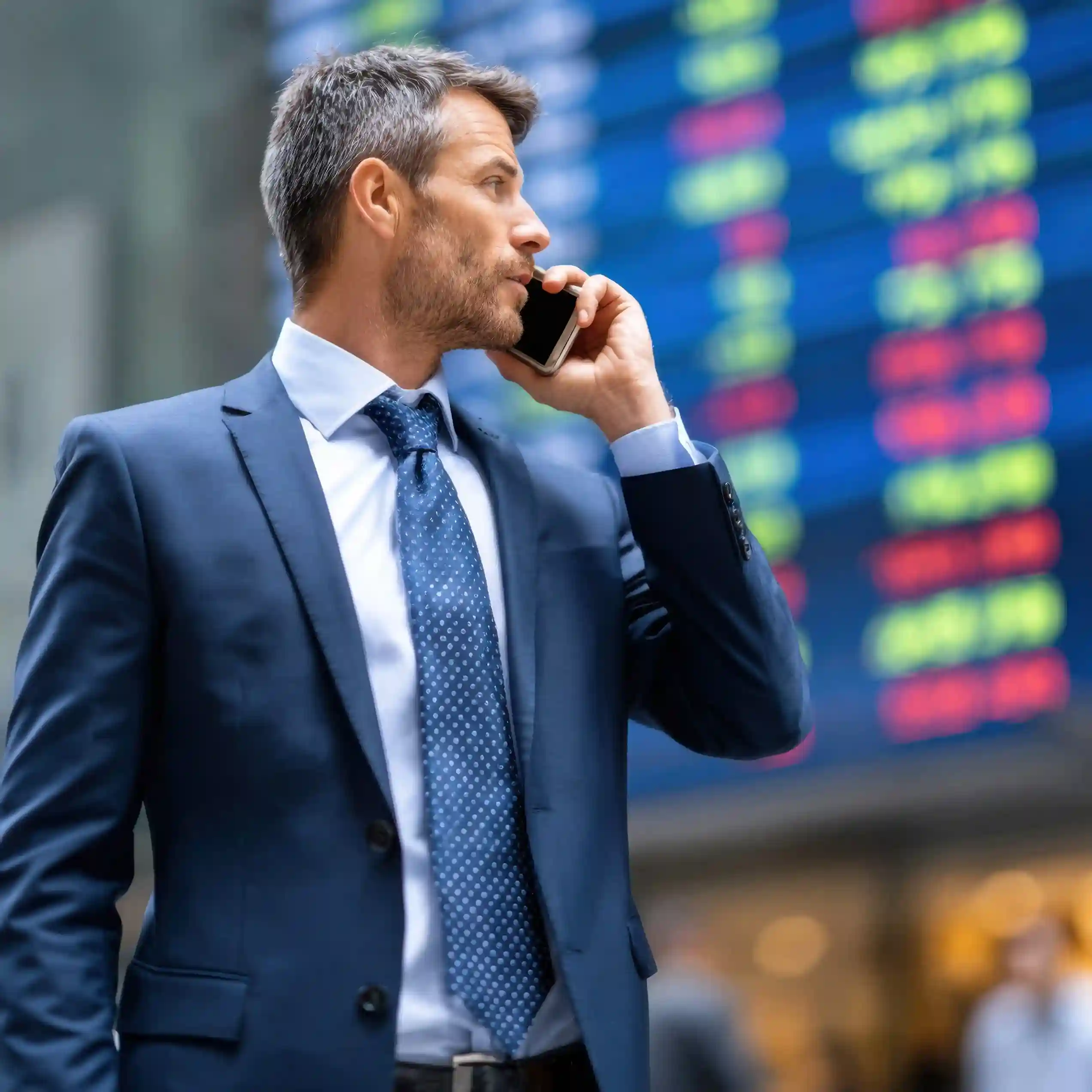 Indosoft helps finance professionals connect securely with clients, manage communications efficiently, and stay informed with real-time financial insights. A businessman in a blue suit communicates with clients via phone using Indosoft’s financial platform, with a digital market board behind him.