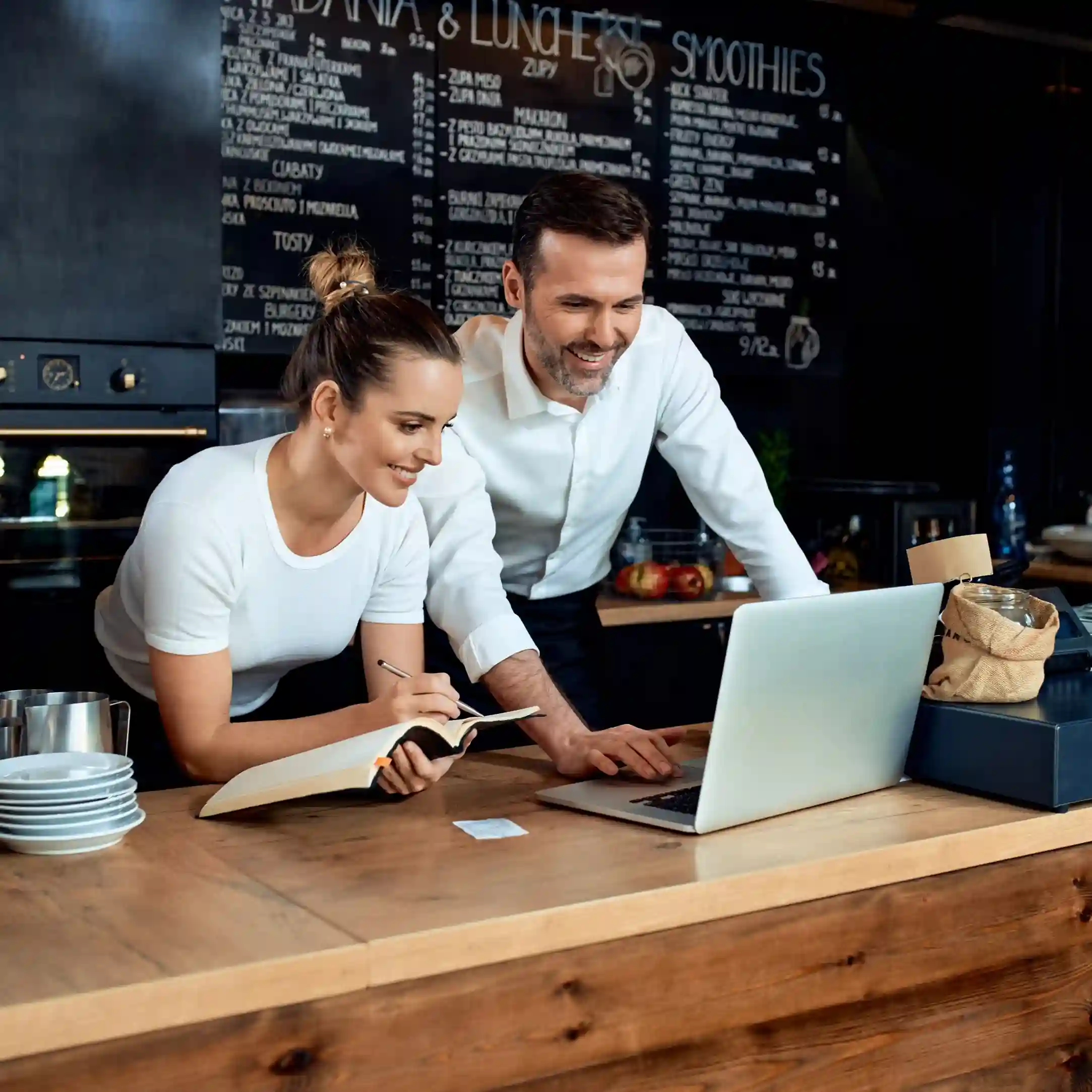Smiling small-business owners in a coffee store using Indosoft to manage sales and drive customer loyalty. Happy café owners reviewing sales on a laptop powered by Indosoft, planning growth and new features.