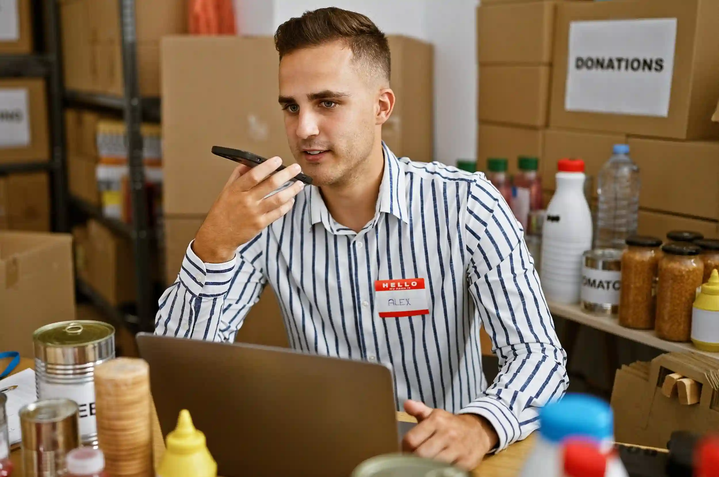 Young man using mobile communication tools in a donation center to handle time-sensitive inquiries. Volunteer using a smartphone among donation boxes to route high-priority messages and improve response times.
