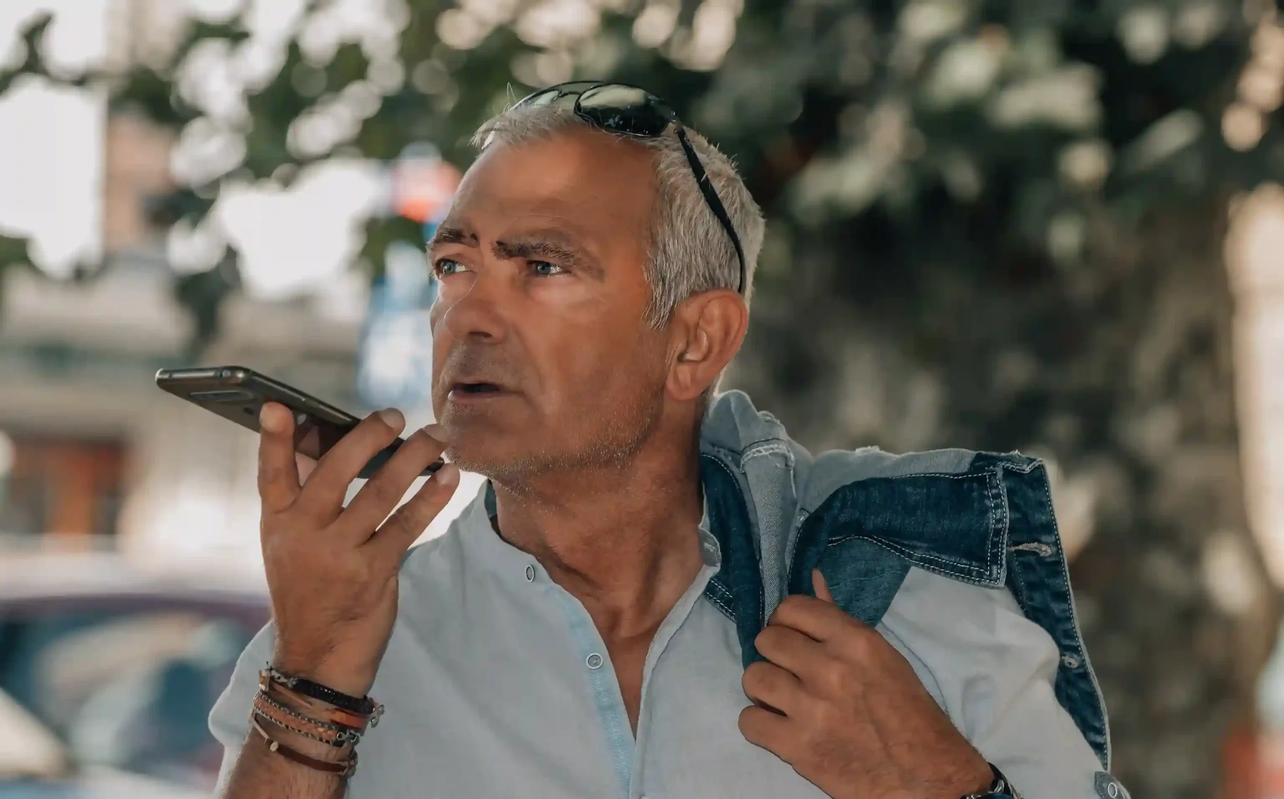 An older customer records a voicemail on their phone in the evening, confidently leaving a service request knowing it will be reviewed the next business day. A senior customer speaks into their phone outdoors after business hours, leaving a clear voicemail request that will be captured and handled when agents return.