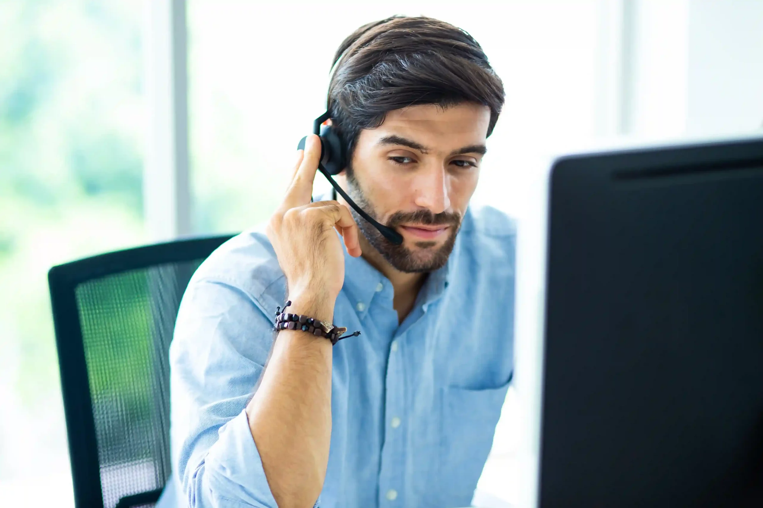 A customer support agent briefly pauses a live call using Indosoft while checking information on his screen to ensure an accurate response. An agent wearing a headset places a caller on hold using the Indosoft solution, taking a focused moment to verify details before continuing the conversation.