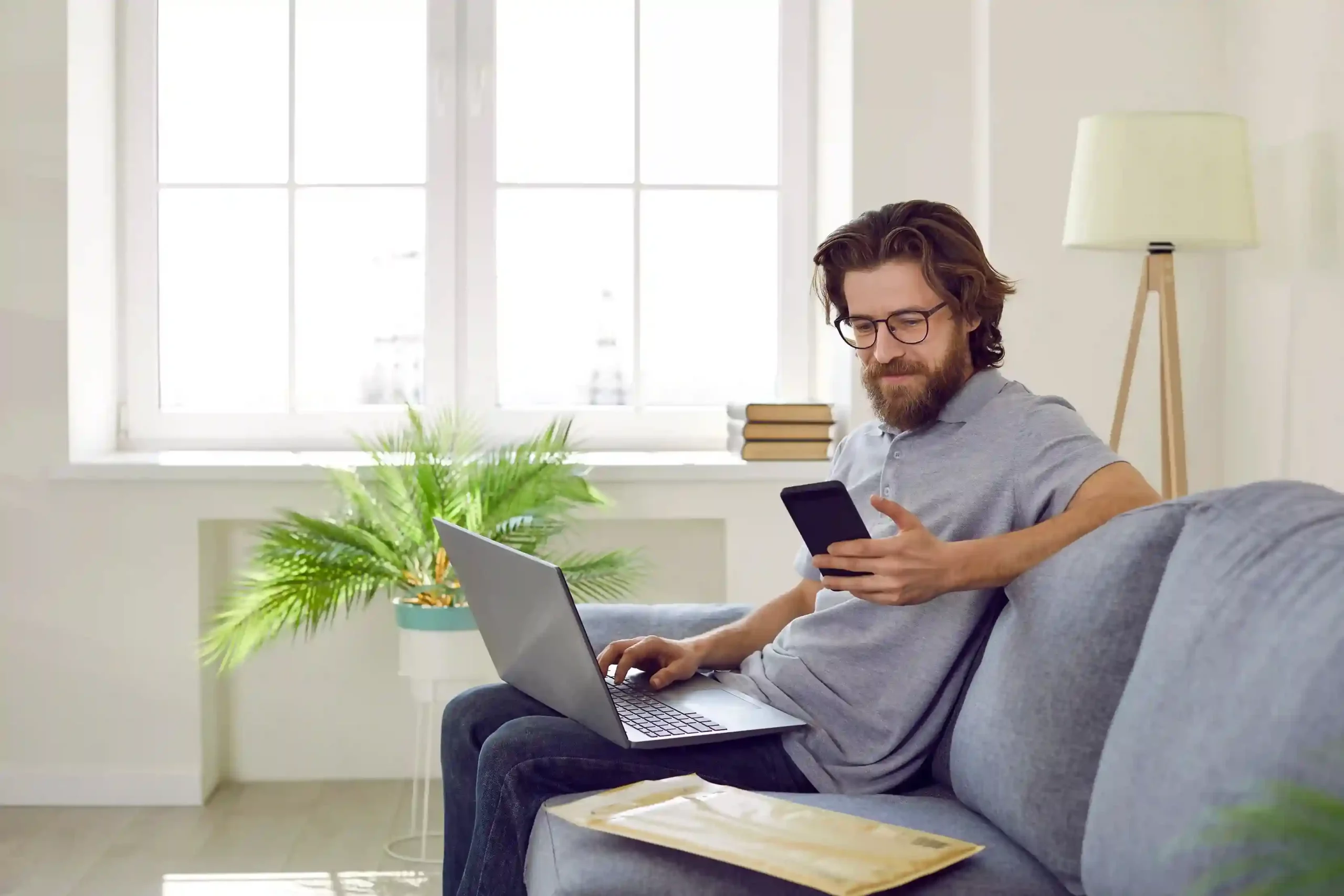 While managing tasks from home, a professional receives a delivery confirmation text that arrives automatically, showing how shortcode workflows handle routine updates without human intervention. Working from his couch with a laptop open, an employee checks a delivery update on his phone, receiving an automated SMS that confirms shipment without needing to contact support.