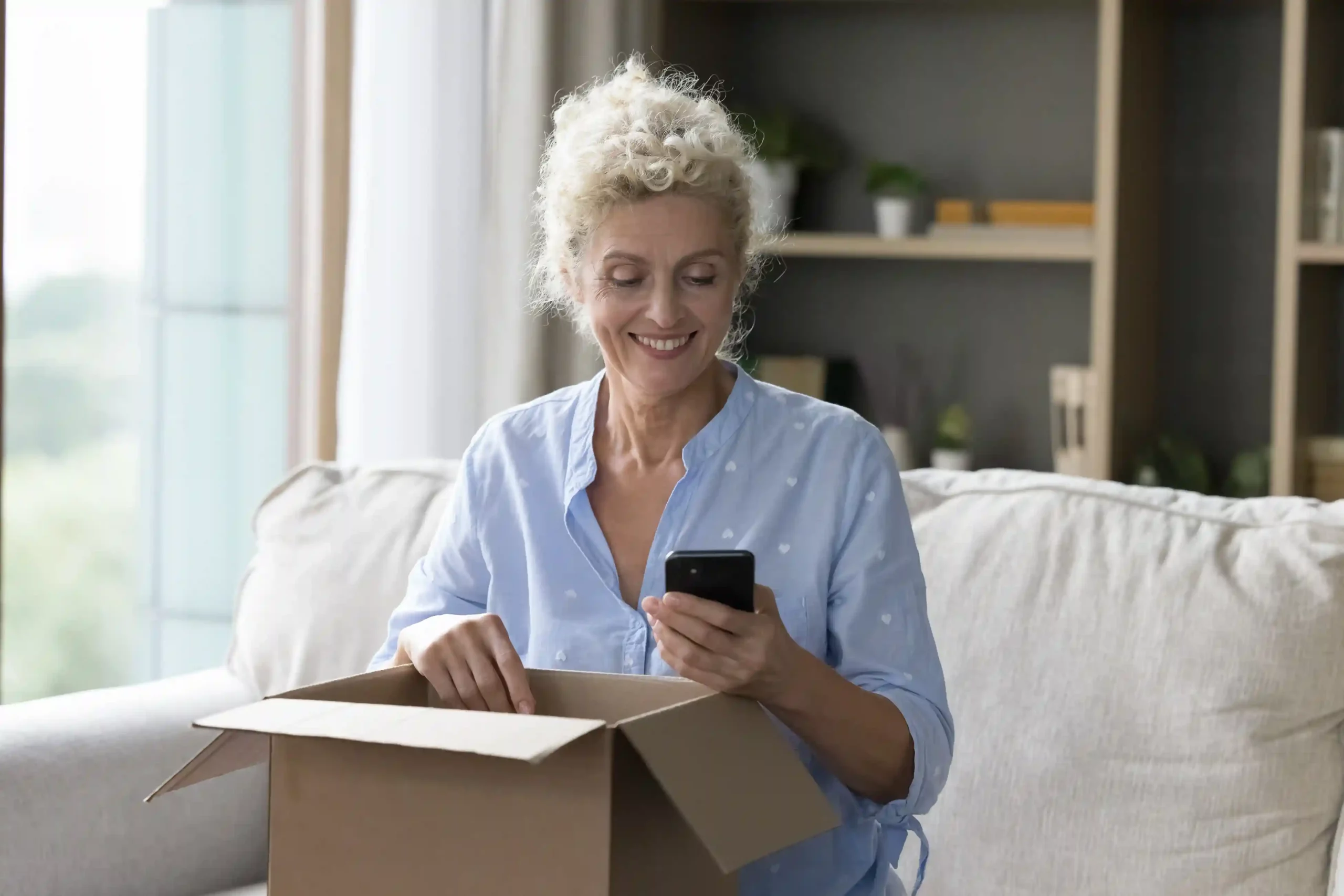 A woman confirming automated SMS timing on her mobile phone during a routine delivery at home. A customer checking scheduled message notifications on her smartphone while managing deliveries at home.