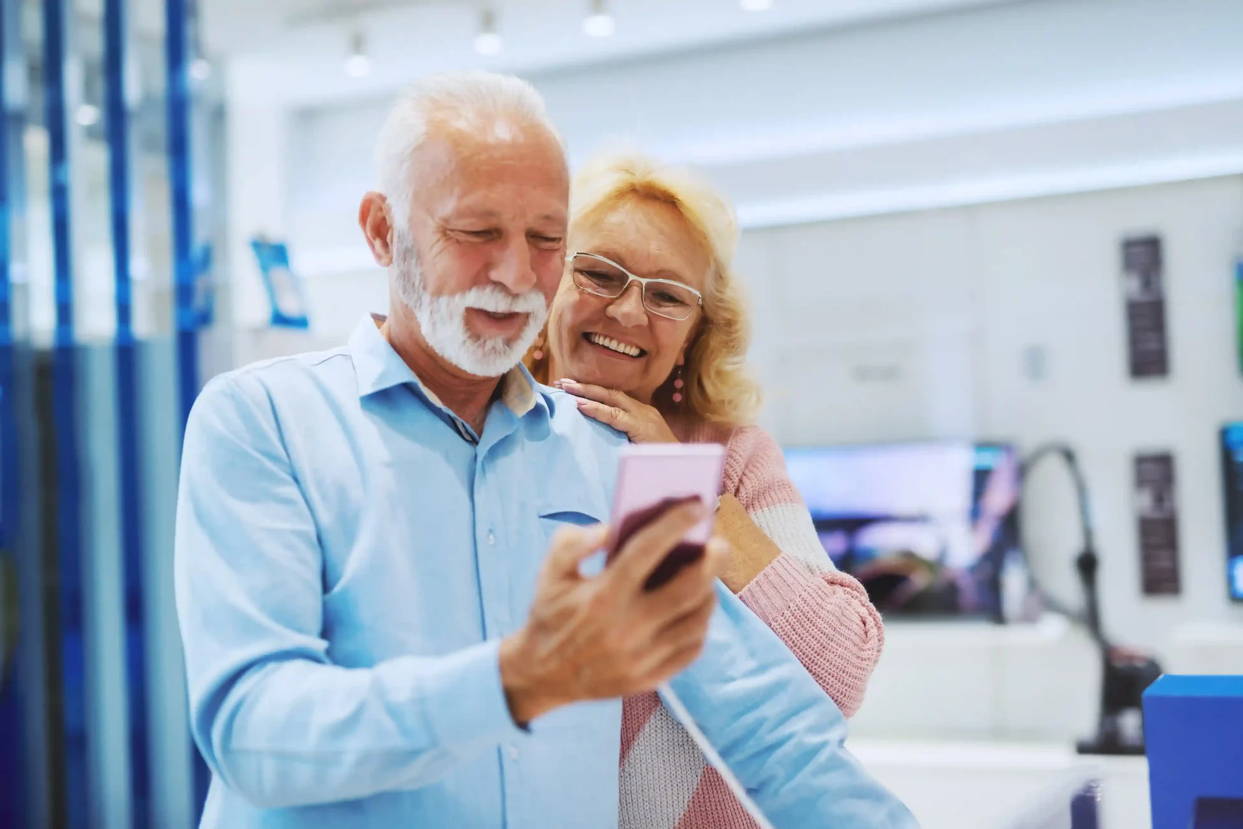 An older couple listens attentively to a customized phone message, feeling reassured by clear, friendly hold audio powered by Indosoft. A senior couple smiles while listening to a phone message, experiencing calm, personalized hold music delivered through the Indosoft call hold solution.