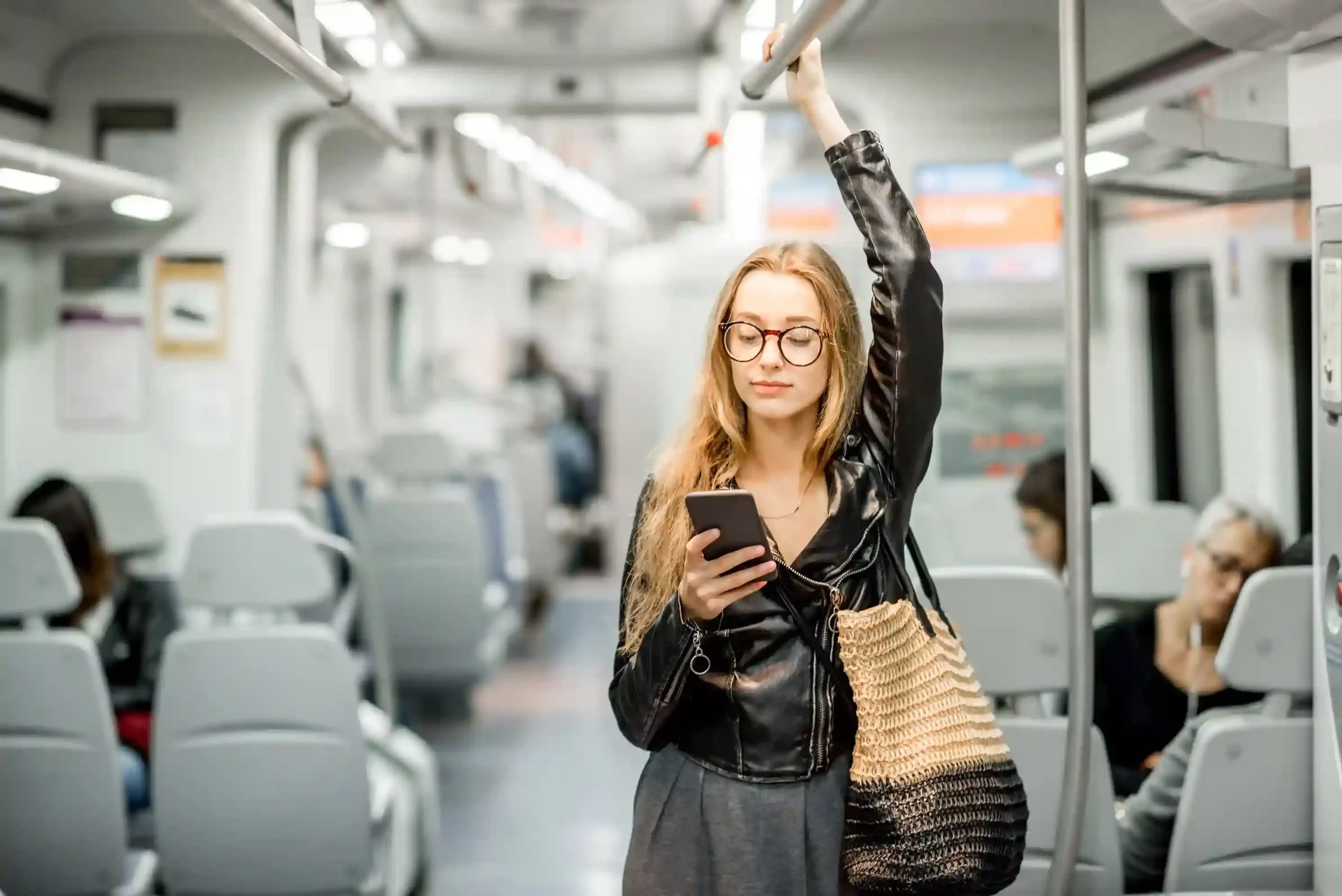 A woman standing in public transit reviews a call notification, reassured by a branded caller ID that clearly identifies the business reaching out to her. A commuter checks an incoming call on her phone during a train ride, recognizing the business name on the caller ID and confidently deciding to answer.