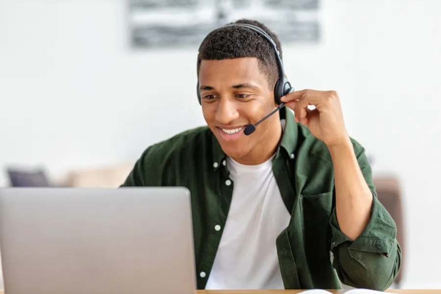 Agent using a headset to manage calls with automated call-routing. Call center agent smiling while managing customer calls on a laptop, demonstrating automated call forwarding based on agent availability.
