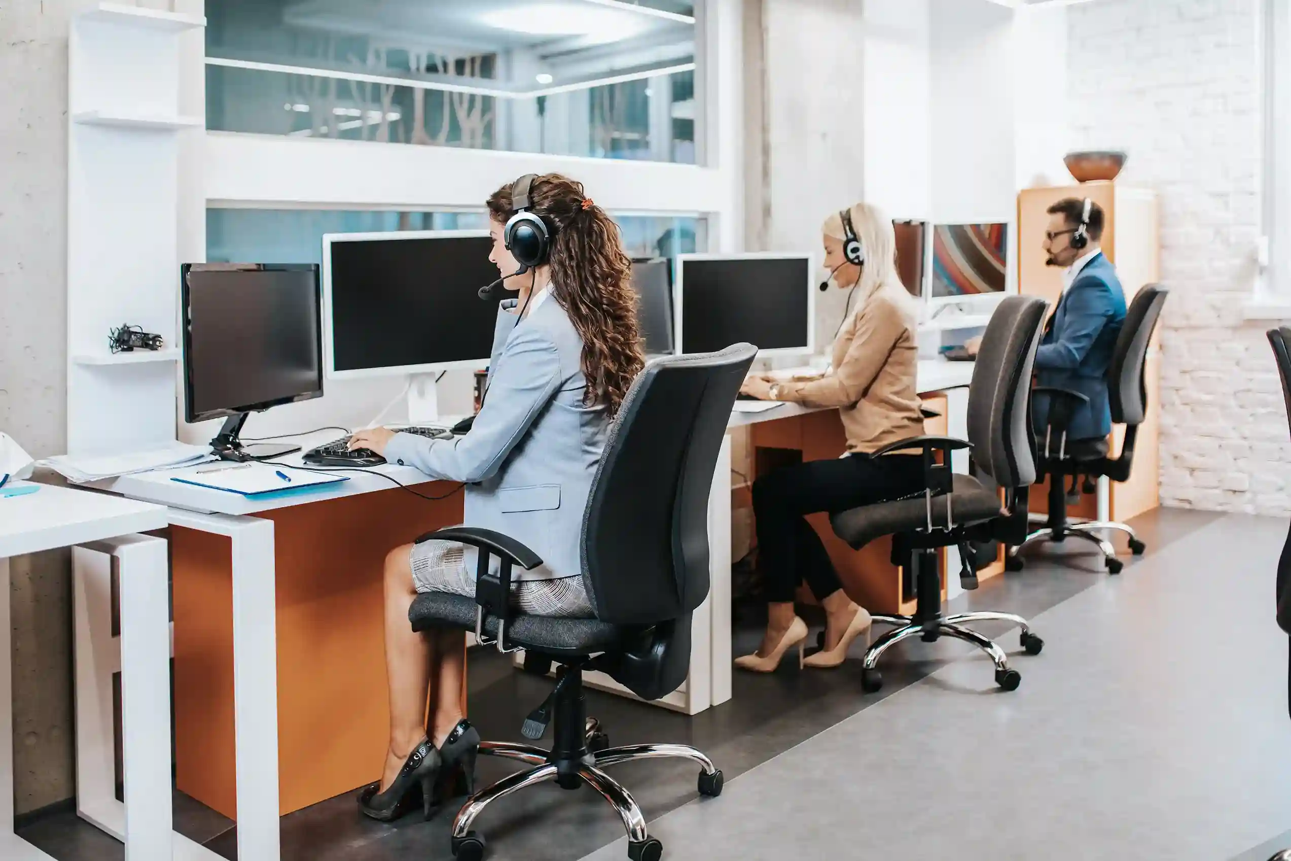 Support agents using headsets in a structured call environment with custom routing options. Call center agents working at their desks with headsets, representing customizable call-forwarding rules tailored to different workflows or departments.