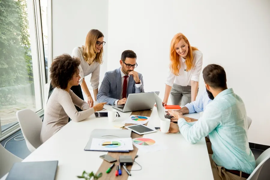 Team meeting with laptops and charts, symbolizing uninterrupted business operations. Team collaborating around a conference table with laptops and charts, representing smooth business operations during staffing or location changes.