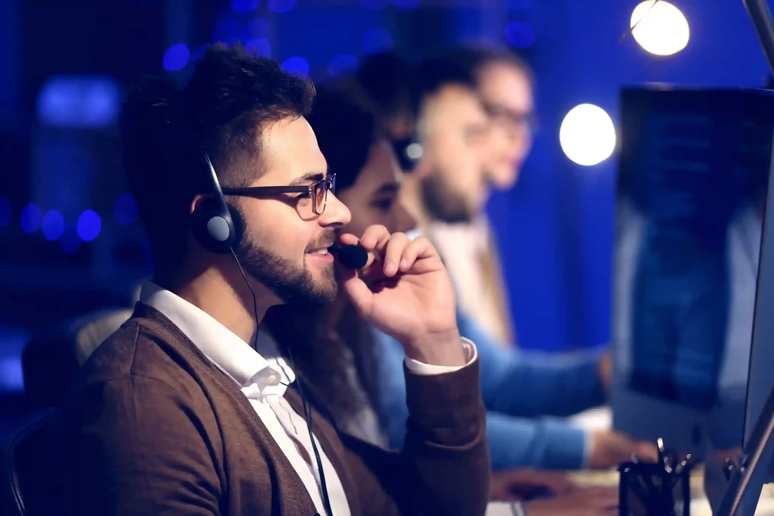 A team lead reviews recorded call details at a workstation, referencing Indosoft call history for compliance and quality checks. A supervisor listens to a past call through a headset, using Indosoft call history to evaluate call quality and guide agent coaching.