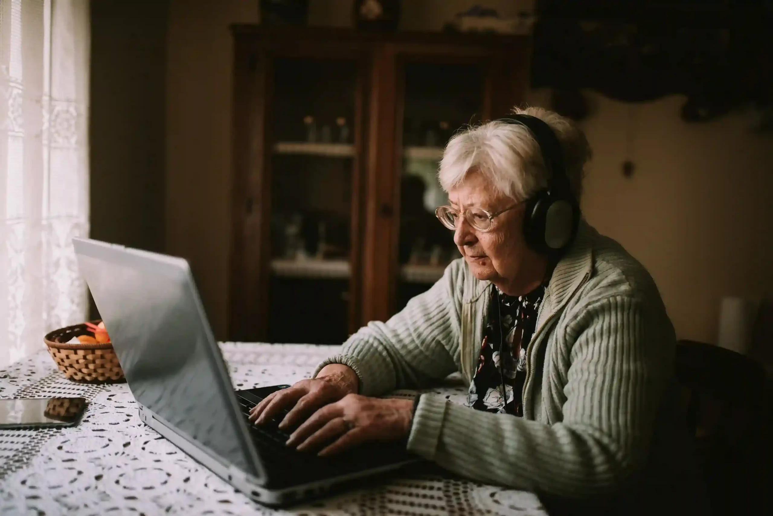 While attending a remote appointment, a senior quietly mutes her audio to manage surrounding distractions, then resumes the conversation clearly when ready to speak. A senior user pauses her microphone during a virtual call with a doctor’s office, using mute to block household noise while reviewing information on her laptop.