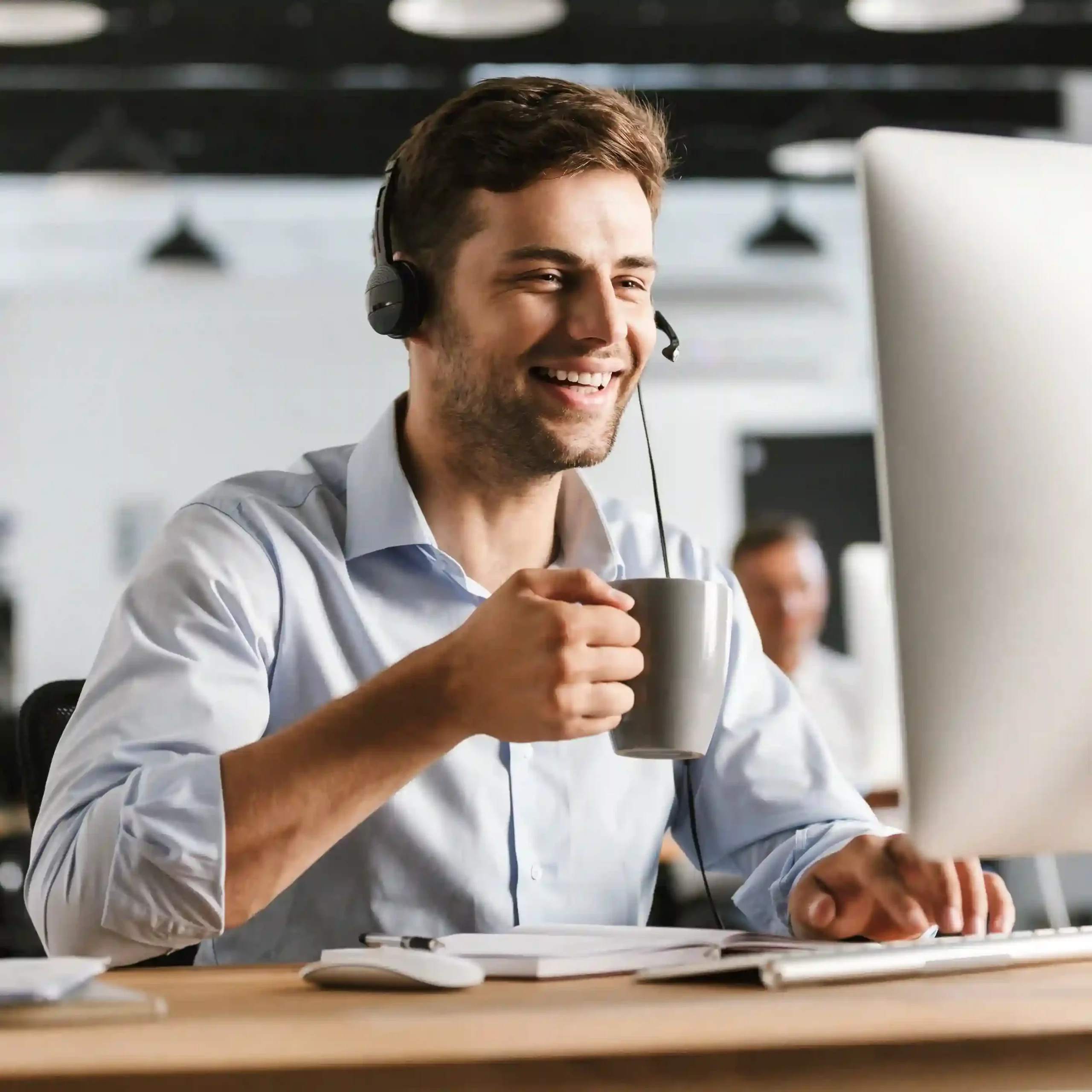 Agent on headset at computer, representing Indosoft’s team helping organizations choose the right call center capabilities. Call center agent smiling while speaking through a headset and working at a computer, representing Indosoft’s expert team helping organizations explore powerful call center features, automations, and integrations.