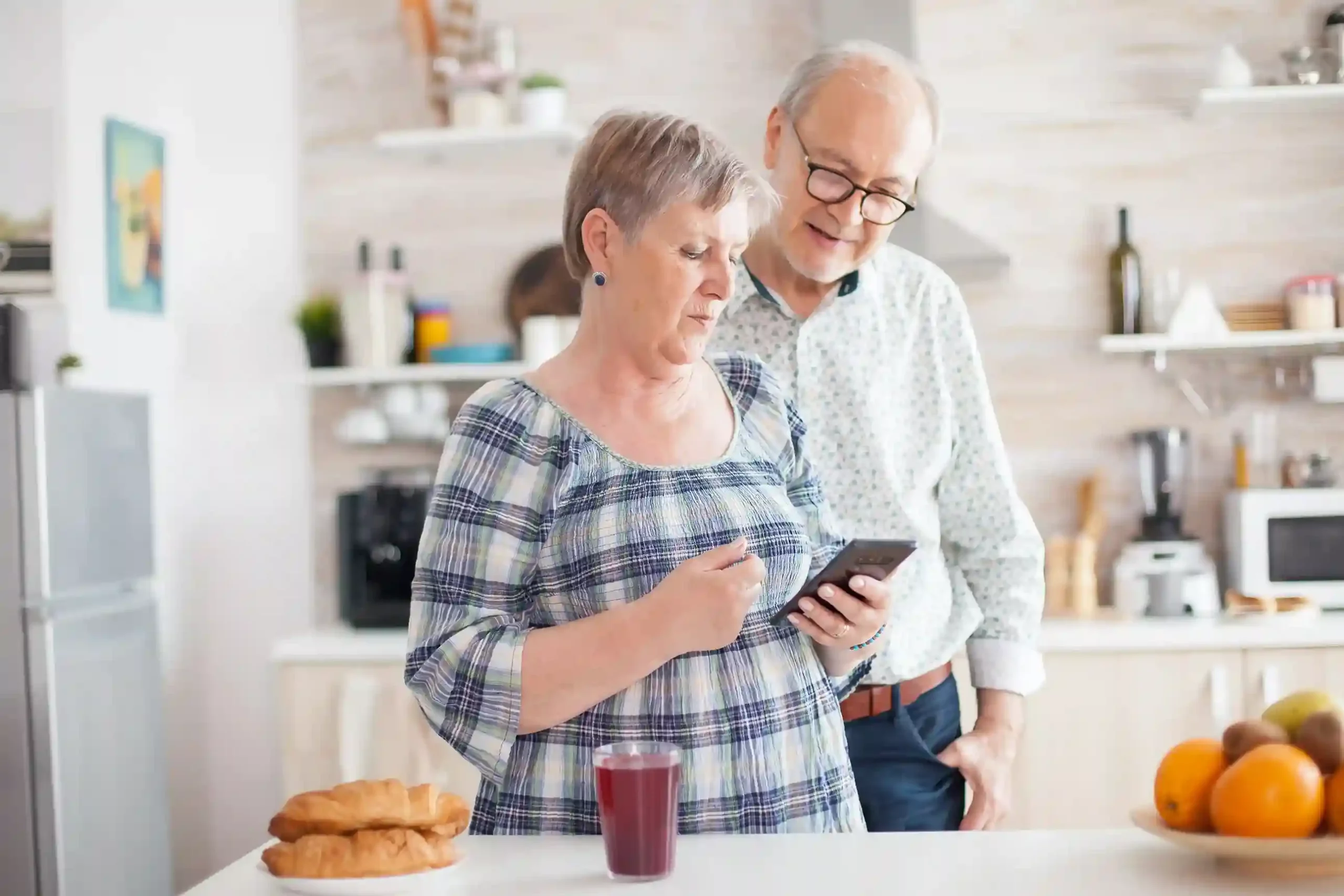 A senior couple calmly follows up on a grocery delivery as their call moves between agents with full context, illustrating a smoother experience without repeated explanations. An elderly couple reviews their grocery delivery details on a phone while continuing a transferred call, showing how preserved context prevents them from repeating the same information.