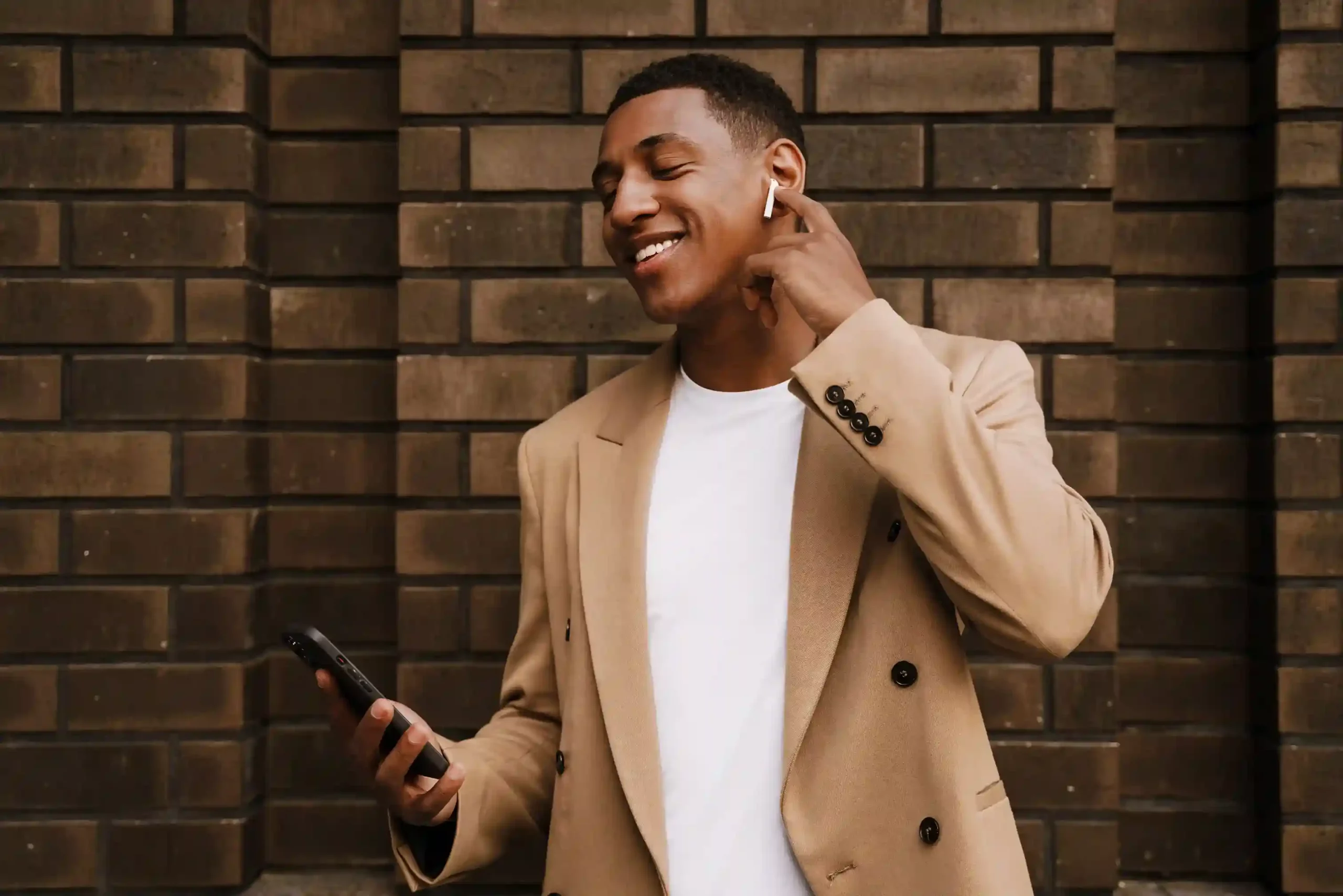 A business user reviews call settings on a mobile device, knowing updated greeting messages will immediately guide callers with the latest information. A professional listens through wireless earbuds while checking his phone, confident that the greeting message has just been updated to reflect a new campaign before callers connect.