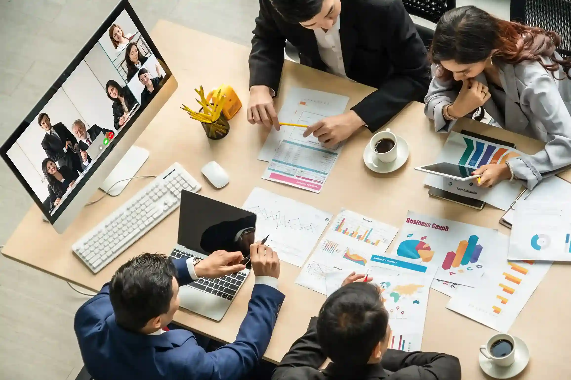 Professionals collaborate around reports and a live video screen, illustrating how agents manage conference participants seamlessly to keep discussions focused and effective. A team reviews live data while joining and adjusting participants on an active conference call, showing how agents bring the right experts into the conversation as needs change.