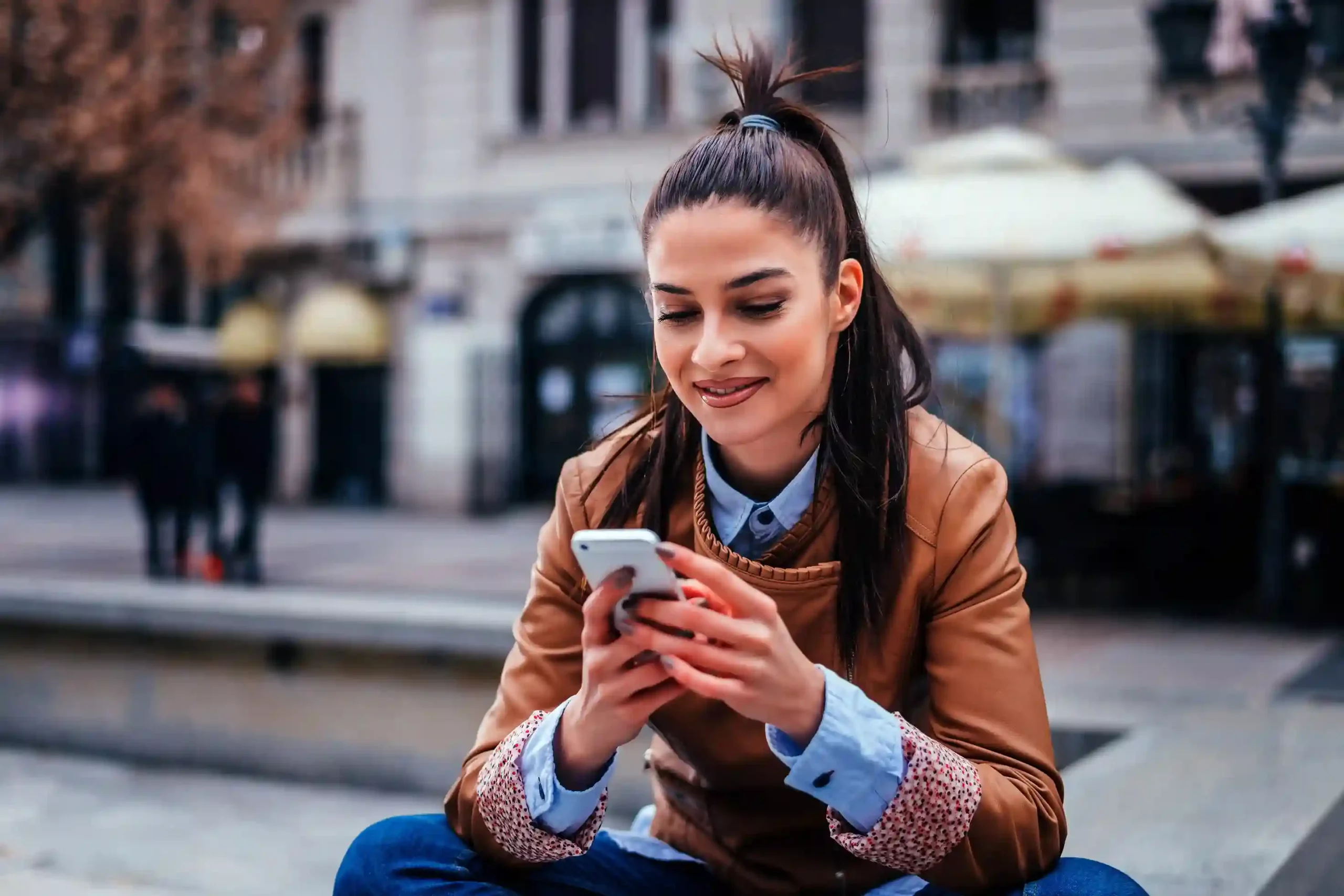 A customer casually reviews a service message on her phone in a public space, picking up the conversation later without restarting the interaction. A customer checks a message on her phone while sitting outdoors, continuing a support conversation at her own pace without staying on a call.