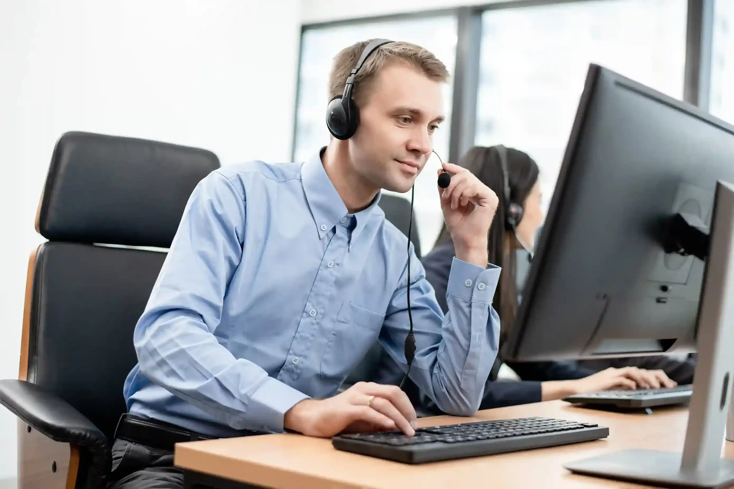 A contact center agent works steadily at his desk, using a unified call interface that keeps the conversation front and center during the call. An agent listens attentively through a headset while managing a live call on one screen, staying fully focused on the conversation without distractions.