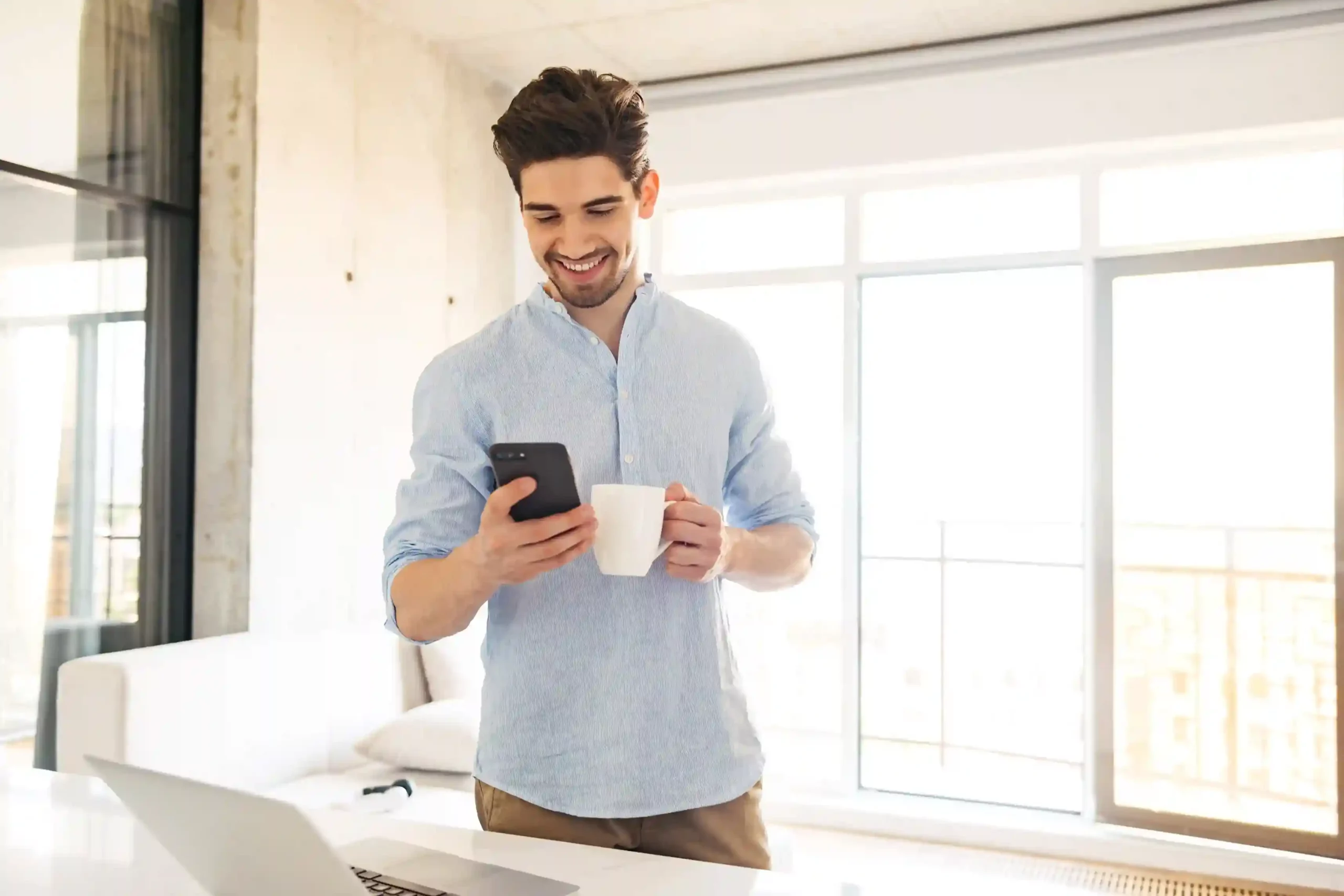 A business professional checks his phone with a smile while holding his morning coffee, showing how Indosoft delivers voicemail messages instantly without interrupting his day with ringing calls A business professional checks his phone with a smile while holding his morning coffee, showing how Indosoft delivers voicemail messages instantly without interrupting his day with ringing calls