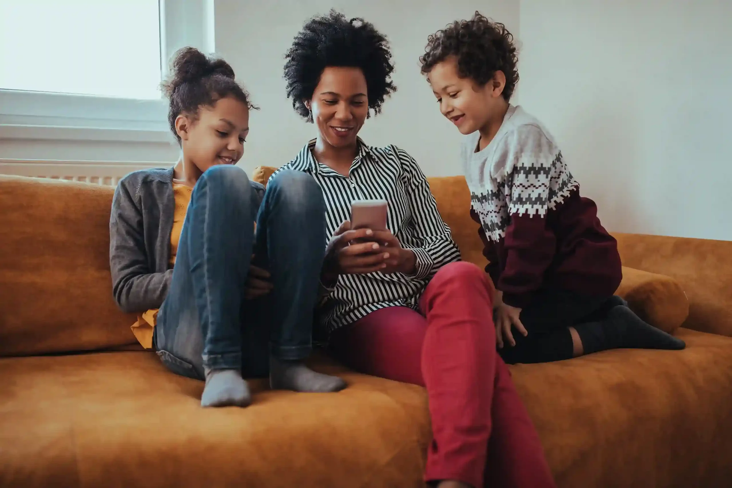 A parent and children relax on the couch after finding the right solution on a phone, mirroring how IVR directs callers efficiently to the correct support path. A family reviews information together on a phone and smiles as their issue is resolved quickly, reflecting how IVR captures caller intent early to speed up resolution.