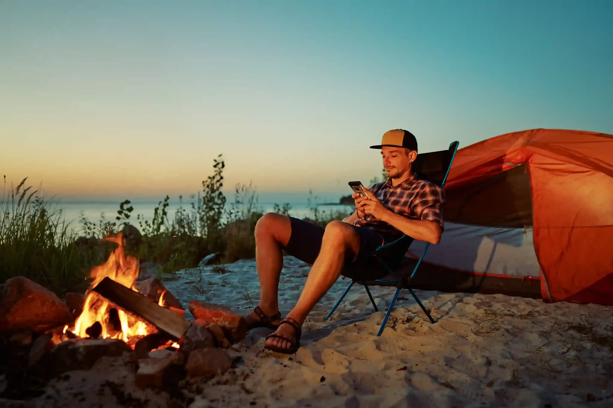 A man reviews a call on his phone during a quiet outdoor moment, noticing a regional caller ID that signals the call is relevant and trustworthy. A traveler relaxes by a campfire while checking a phone message, recognizing a familiar local number on the screen and feeling more comfortable responding.