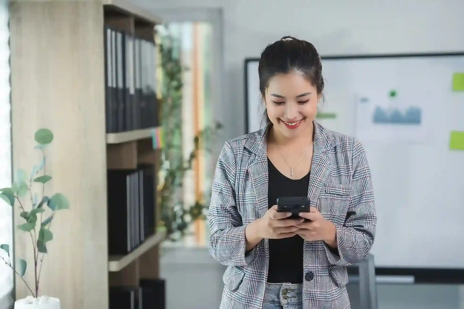 A customer smiles while reading a message on her phone, feeling comfortable engaging with a business that uses a recognizable local number. A professional checks her phone and confidently responds to a business message, knowing the local number makes reaching the company simple and familiar.