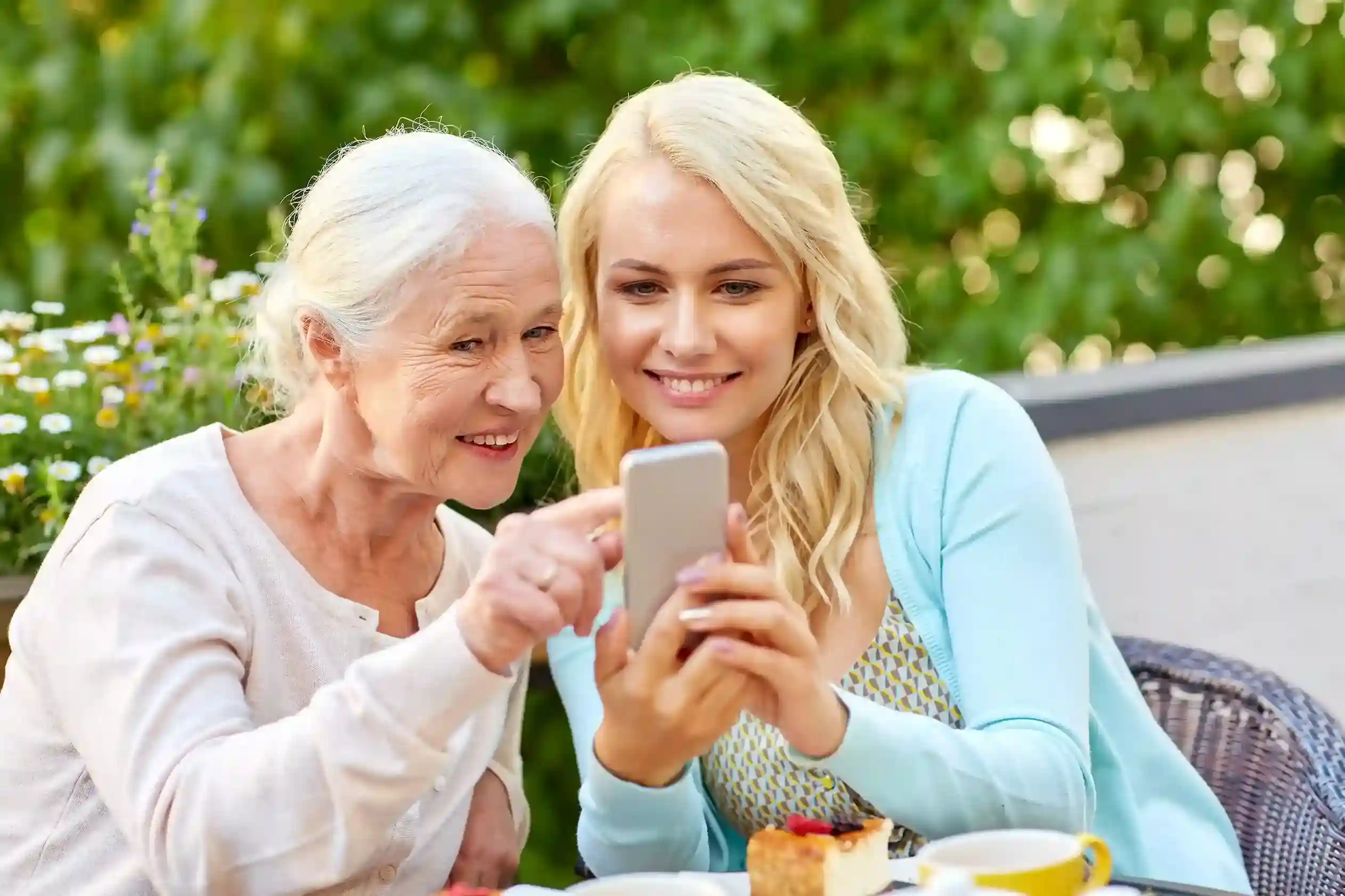 A daughter patiently teaching her elderly mother how to recognize local phone numbers on a smartphone. A daughter showing her mother a phone screen, explaining how local area code numbers help identify trusted incoming calls.