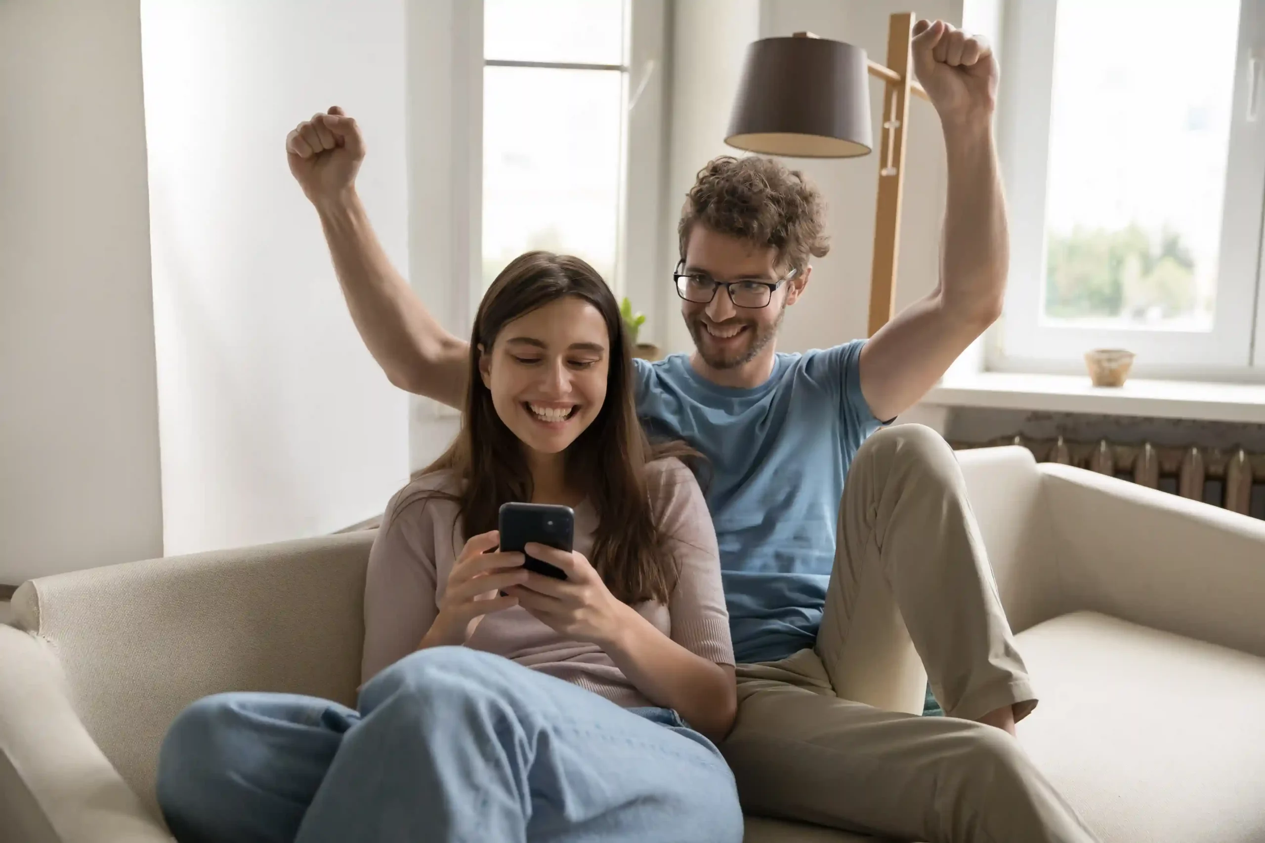 A couple reacts with excitement to a successful booking confirmation on a mobile phone, illustrating how structured call queues support smooth handling even during peak traffic. A couple celebrates on the couch after securing a holiday booking on their phone during a busy period, reflecting how Indosoft’s call queues help businesses stay responsive and stable during peak demand.