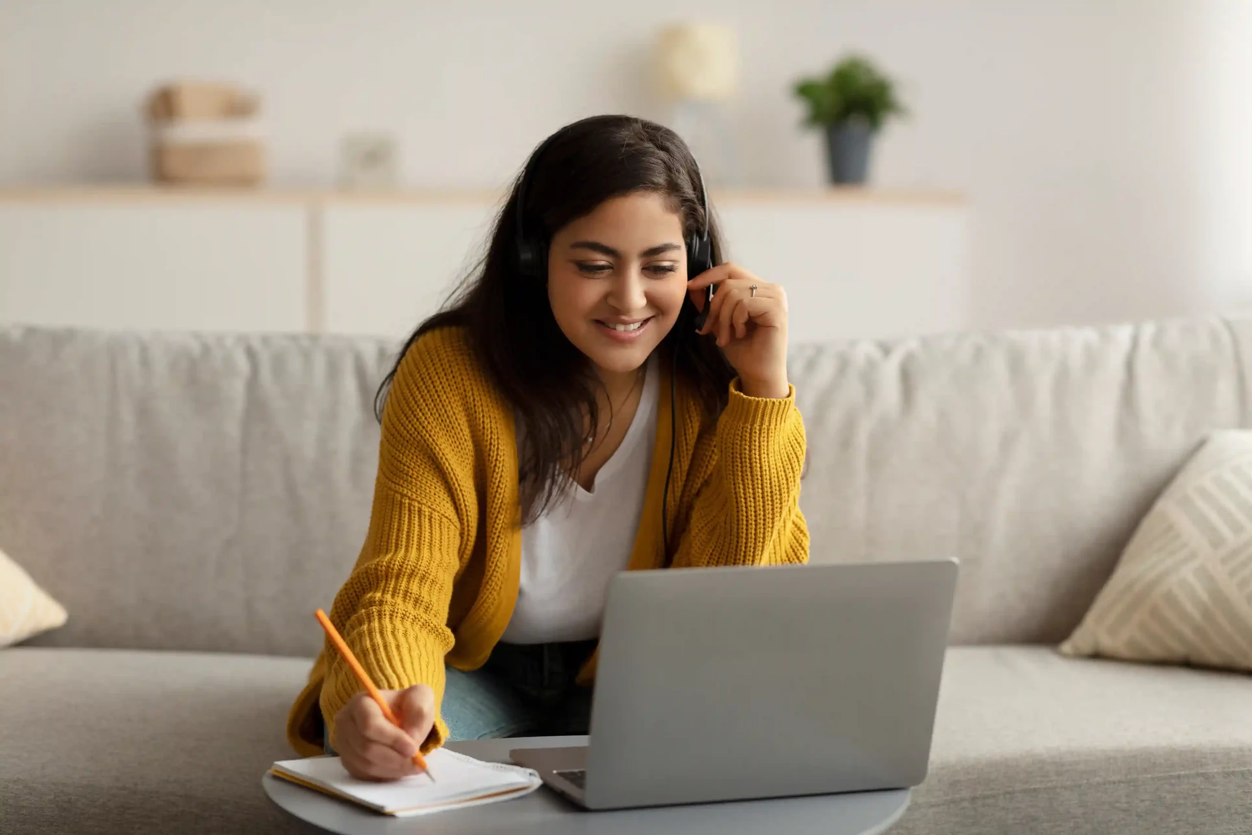 A learner attends a virtual lesson from her couch while the system manages incoming calls smoothly, showing how structured call handling keeps experiences reliable without interruptions. A student focuses on her online class while taking notes on her laptop, trusting that incoming calls are handled consistently in the background without disrupting her study time.