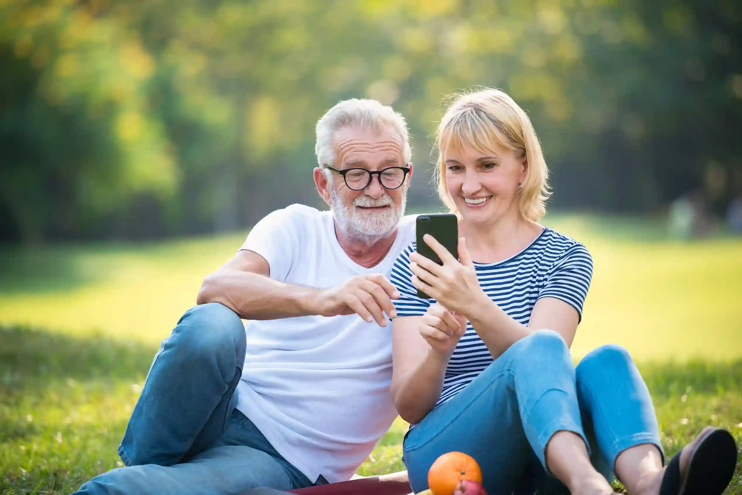 While relaxing outdoors, an older couple calmly reviews a single SMS, benefiting from message rules that block distractions and surface only important information. An elderly couple sits together reviewing a message on a phone, relieved to see only meaningful updates after unnecessary SMS have been filtered out.