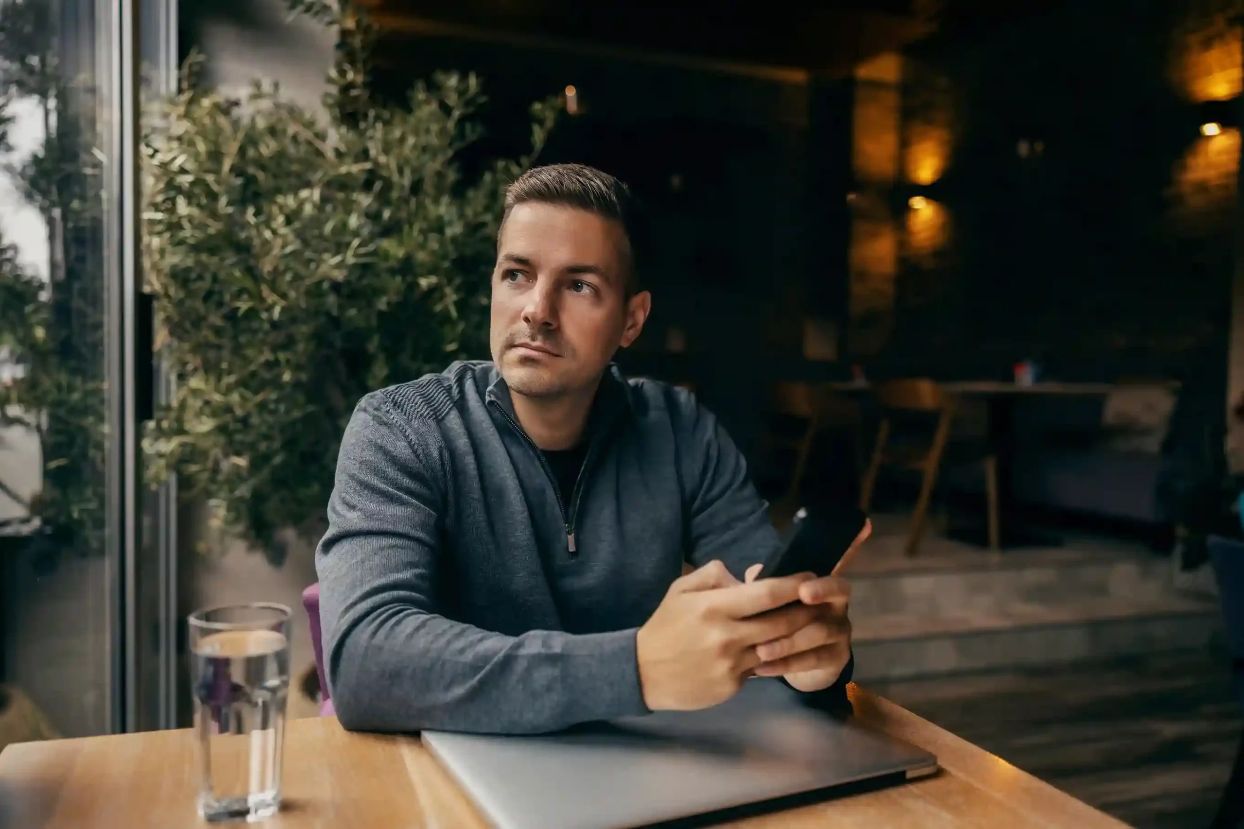 A team member pauses to check his mobile device, relying on Indosoft to monitor the progress of open conversations as they move toward resolution. A professional reviews conversation updates on his phone while seated at a café, using Indosoft to track how quickly customer conversations move from open to closed.