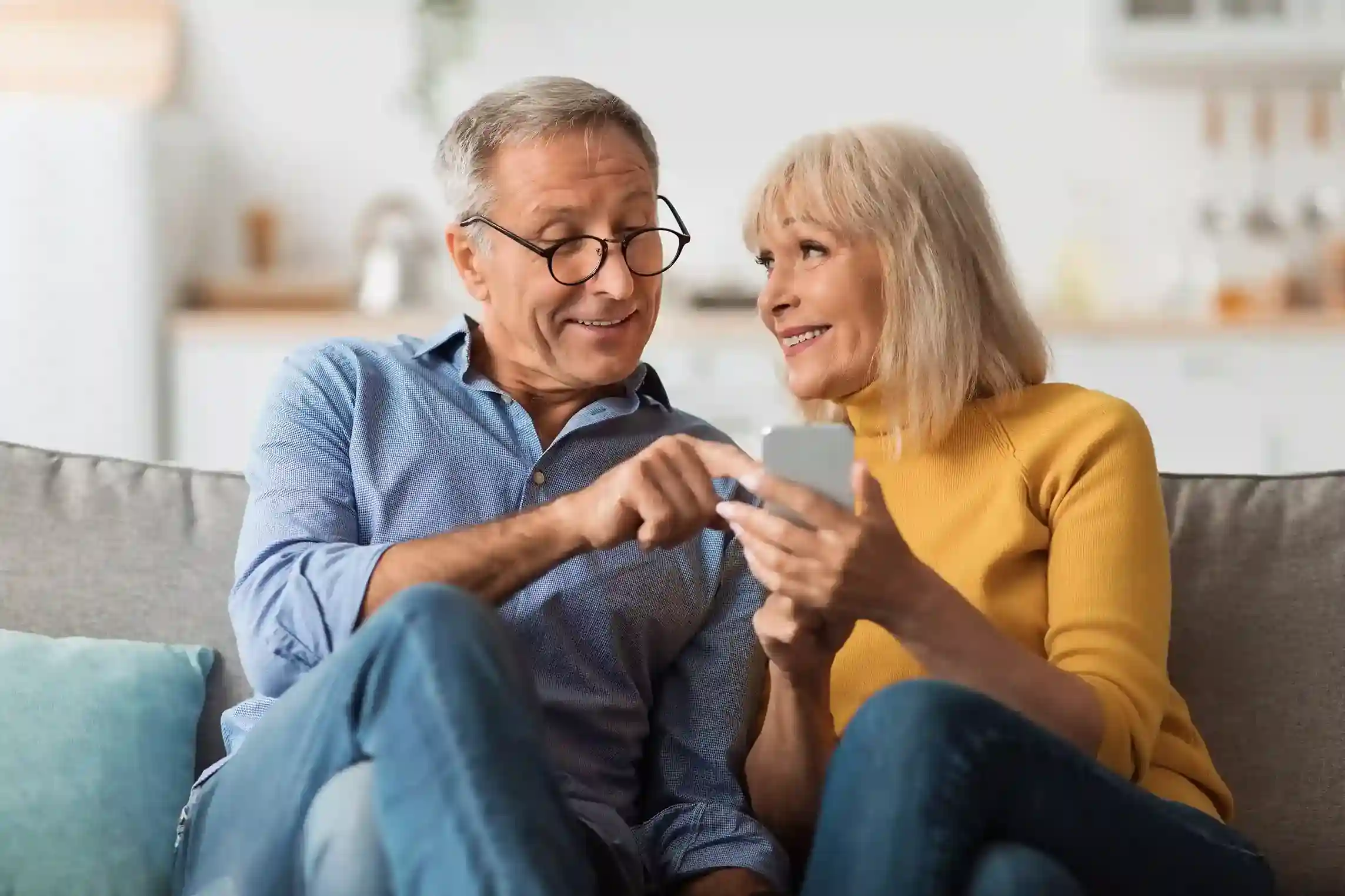 Looking at a campaign message on a smartphone, a senior couple discusses information sent through a large-scale SMS outreach managed with filtering controls. A senior couple reviews an informational SMS together at home, receiving a campaign message that was delivered efficiently to a broad audience through filtered SMS rules.