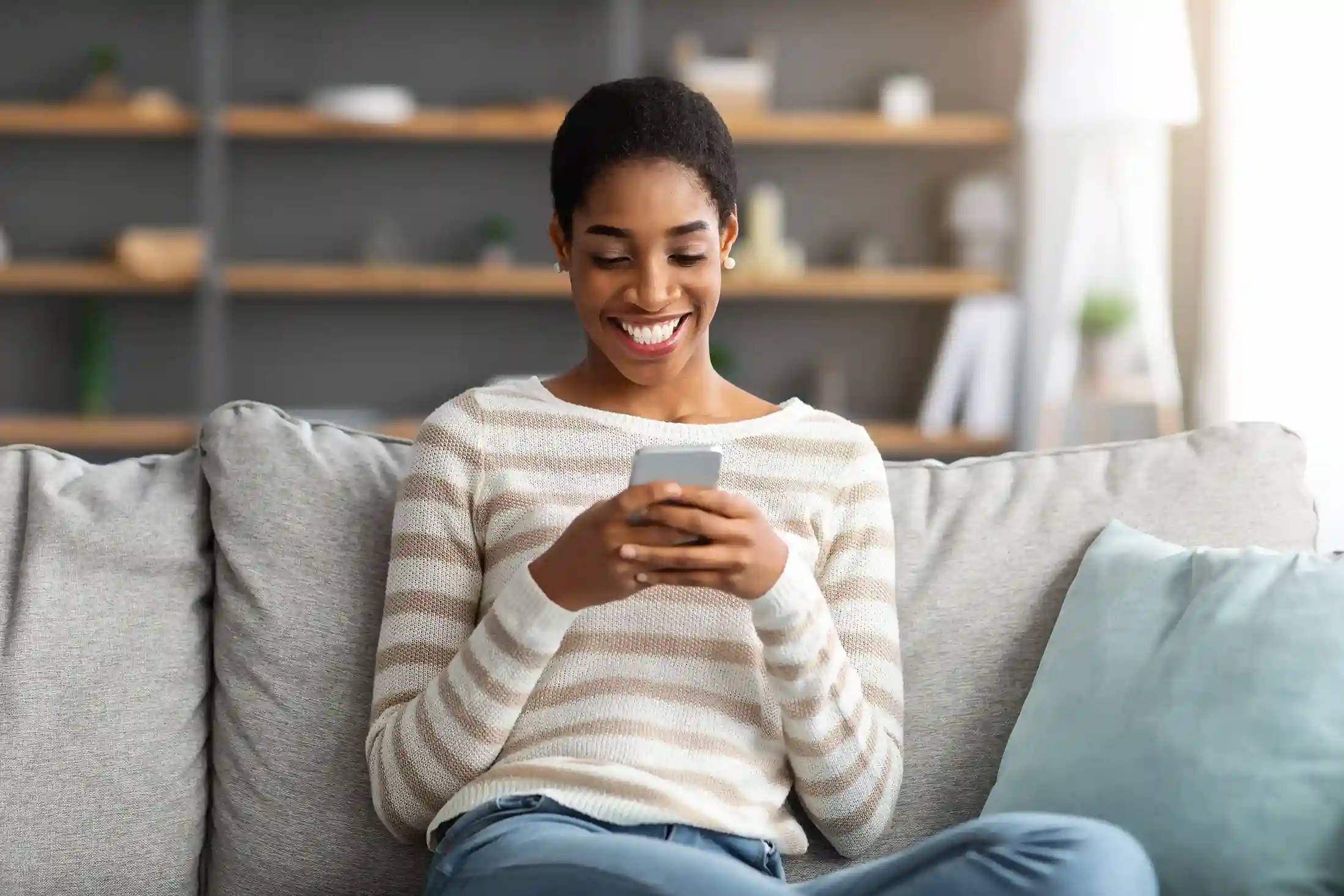 A customer checks a thoughtfully timed MMS on her phone at home, illustrating how scheduled visual messages arrive at the right moment with helpful context Relaxing at home, a customer smiles while viewing a scheduled MMS update sent in advance, showing how planned visual messages keep communication timely and engaging