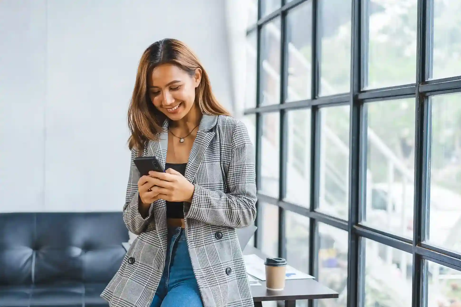 While taking a short break at work, a business professional reads a scheduled text reminder for an upcoming appointment, delivered automatically at the planned time. Smiling as she checks her phone near the office window, a professional receives a timely appointment reminder that was scheduled in advance through an automated SMS workflow.