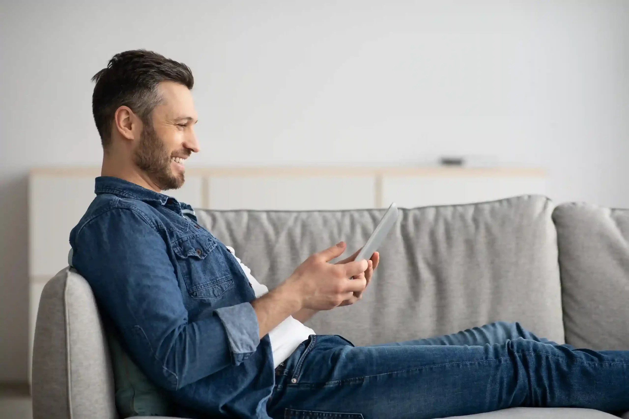 Checking his tablet during a quiet moment at home, a customer receives a timely medication reminder delivered through a pre-scheduled SMS. Relaxing at home on the couch, a customer smiles as he reads a scheduled text reminder about an upcoming dentist appointment sent at the right time.
