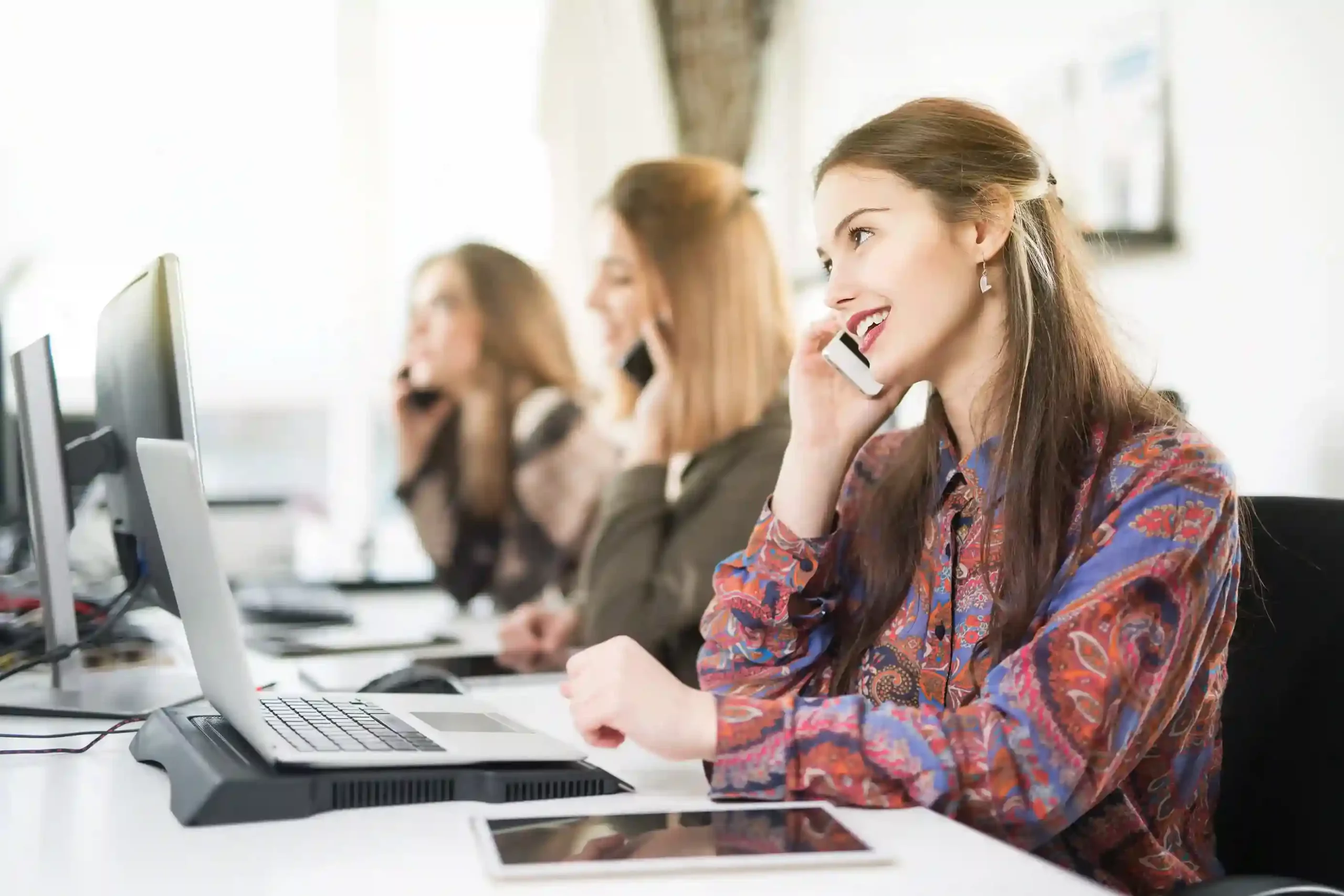 A remote agent wearing a headset smiles while updating call outcome labels on a laptop for consistent interaction tracking. An agent continues assisting a customer while smoothly transferring the call to another team, ensuring the conversation flows without interruption or repeated explanations.