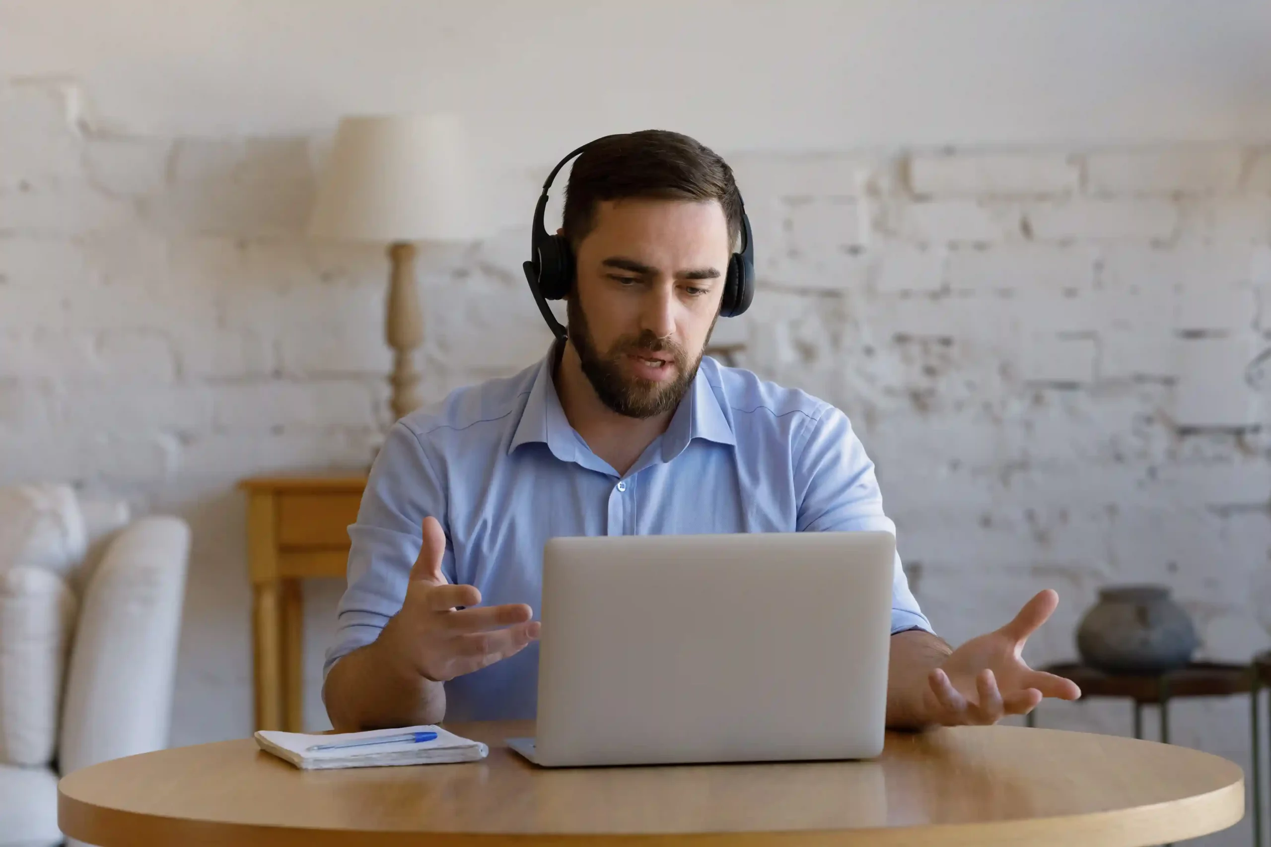 A professional gestures thoughtfully during a live call, referencing centralized customer records to stay coordinated with colleagues. An agent speaks through a headset while reviewing shared customer details on his laptop, ensuring his team stays aligned during an ongoing conversation.