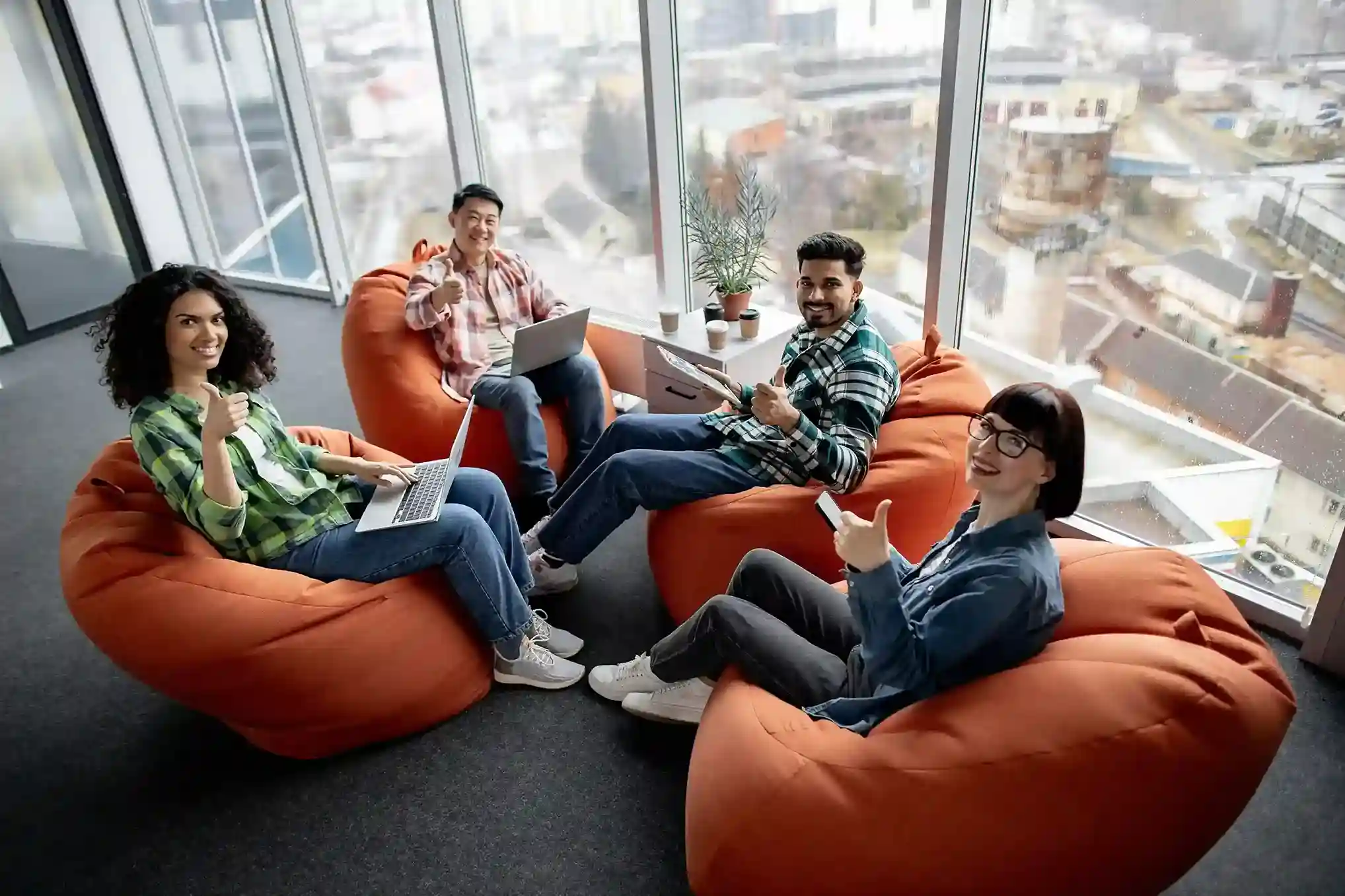 While seated together with devices in hand, a team discusses how to segment contacts so each SMS message reaches the right audience at the right time. A cross-functional team relaxes in a collaborative workspace while reviewing laptops and tablets, planning an SMS campaign by defining audience segments for a new product launch.