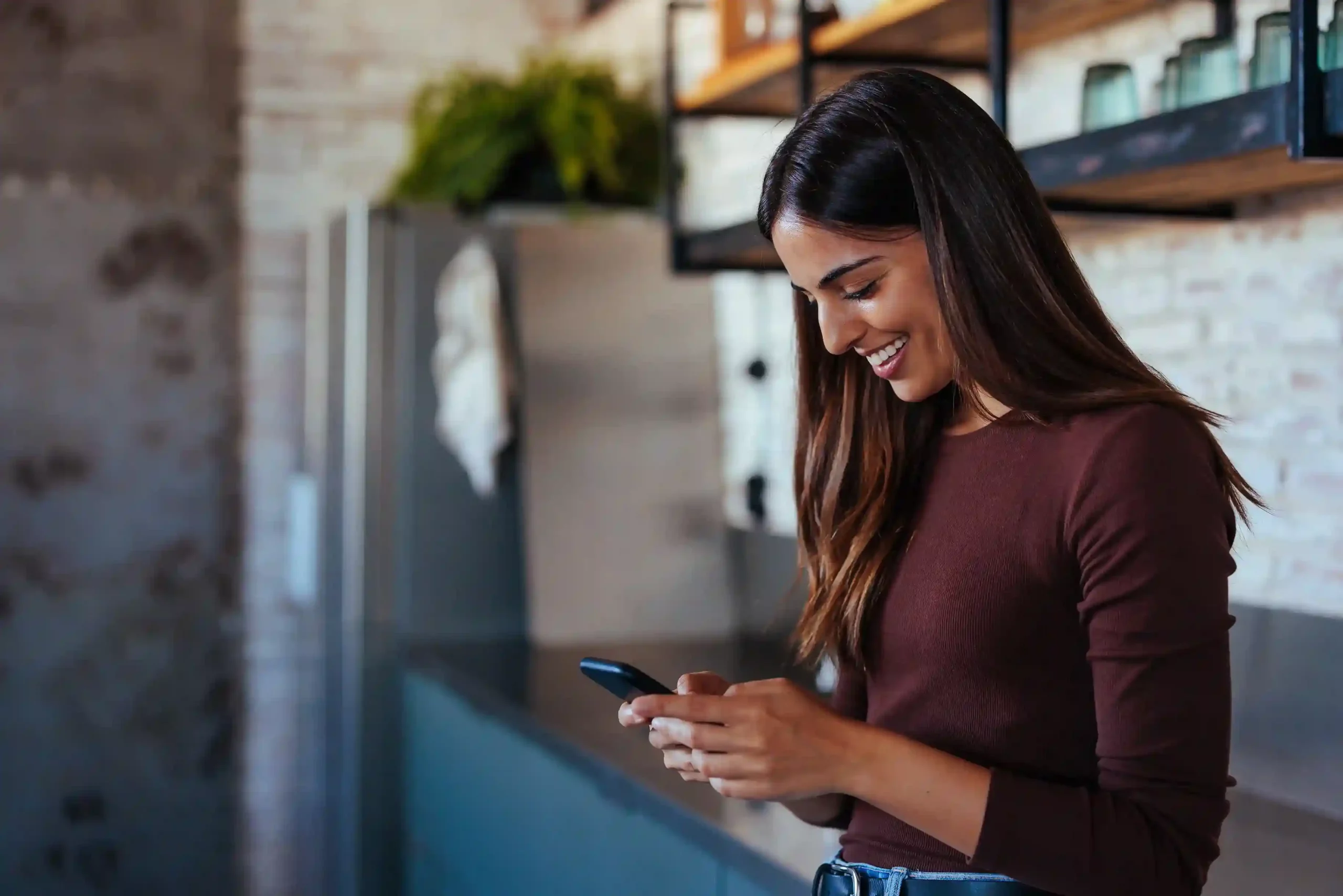 A customer checks her phone in a relaxed setting after receiving a sales update sent through a filtered SMS campaign. At home, a customer smiles while reading a promotional SMS that was delivered through campaign-based filtering to match her interests.