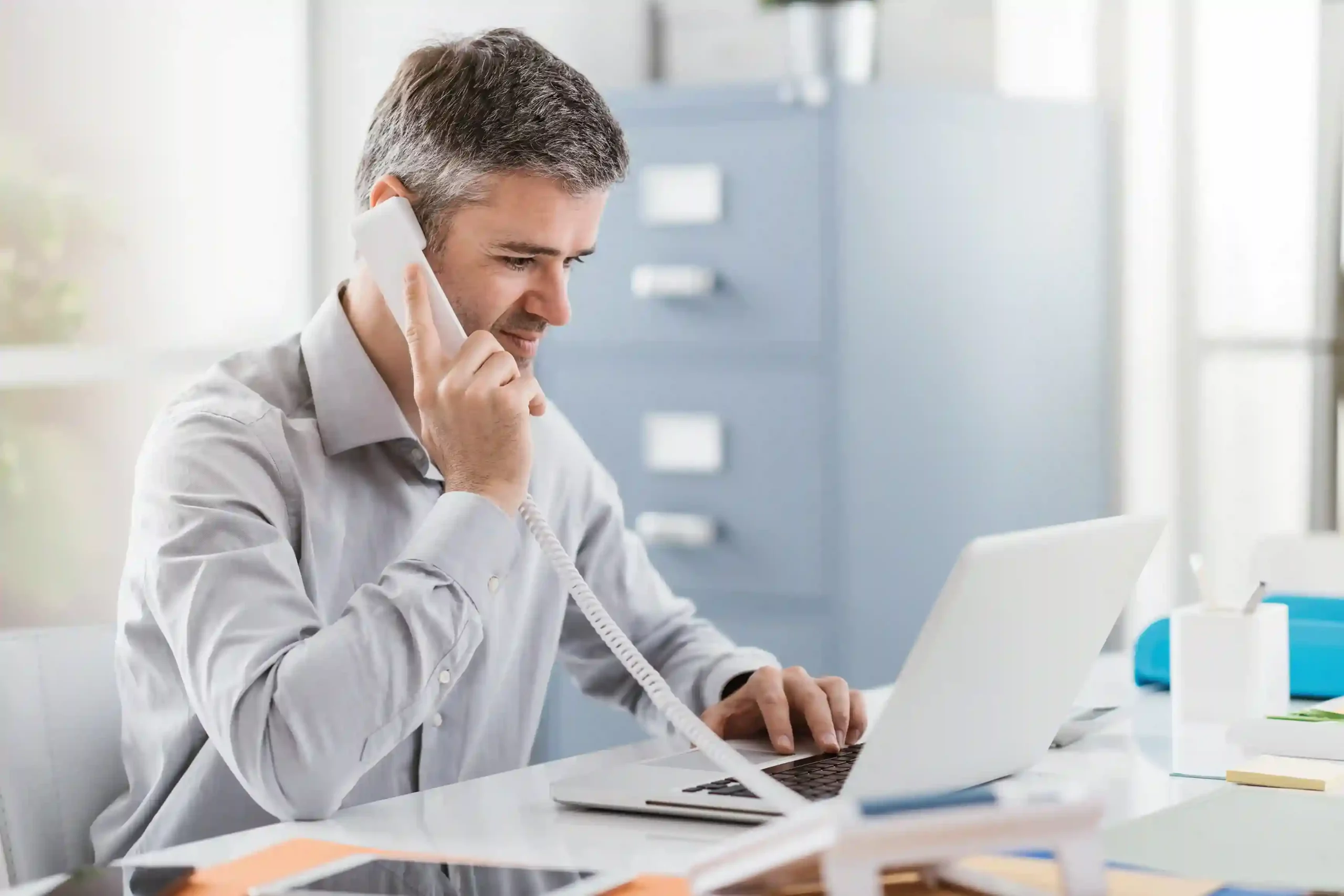 A professional calmly handling calls on his desk phone while time-based call filters ensure only appropriate calls reach his family during off-hour A professional calmly handling calls on his desk phone while time-based call filters ensure only appropriate calls reach his family during off-hour