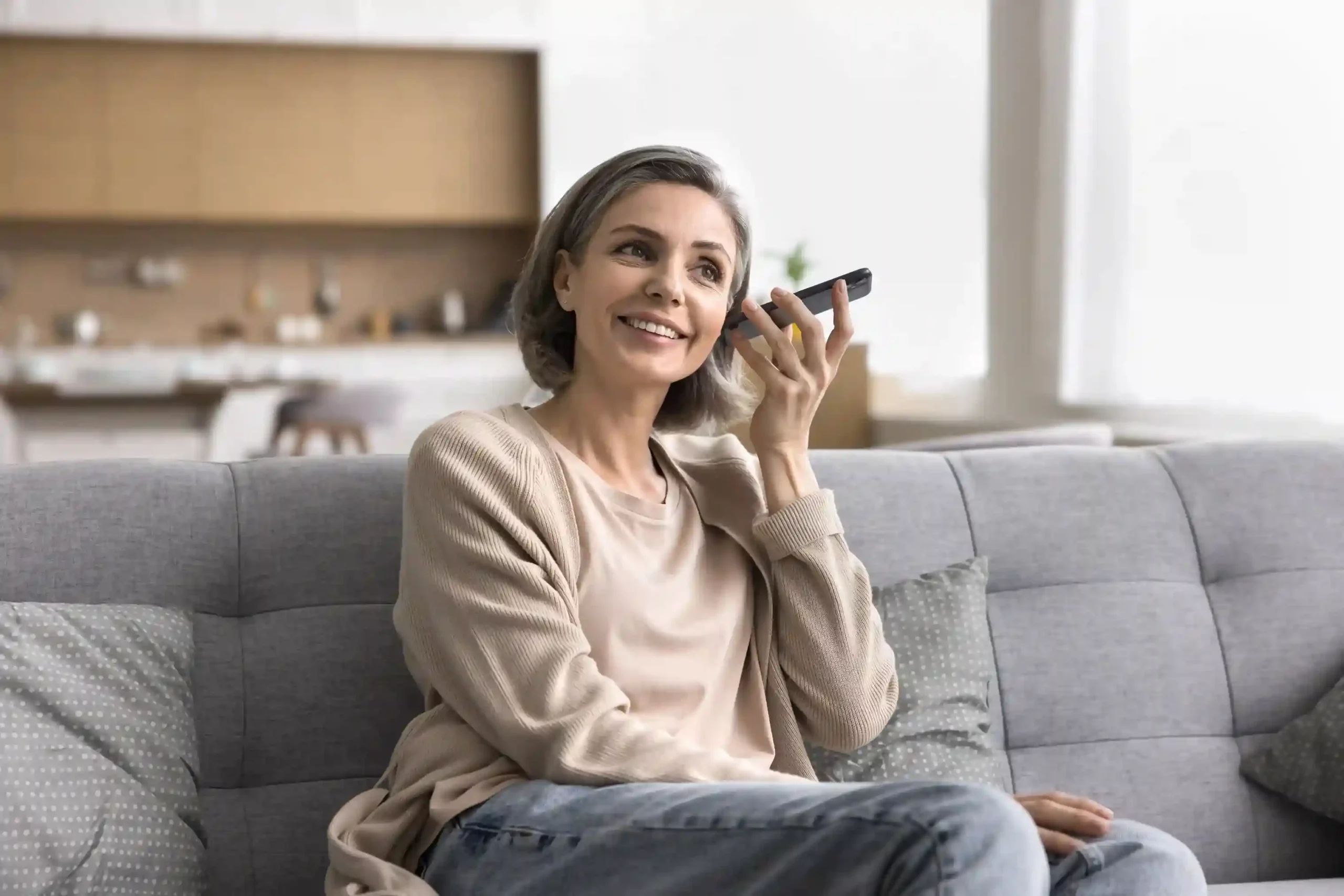 A woman smiles as she plays a voicemail audio attachment from her email, relying on Indosoft to stay connected to missed calls without opening a contact center dashboard. A professional relaxes at home while listening to a voicemail audio attachment on her phone, using Indosoft to review messages directly from email without accessing a call system.