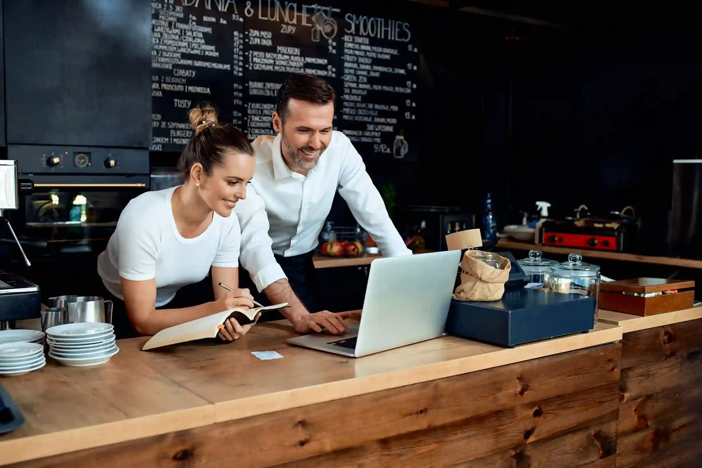 Smiling small-business owners in a coffee store using Indosoft to manage sales and drive customer loyalty. Happy café owners reviewing sales on a laptop powered by Indosoft, planning growth and new features.