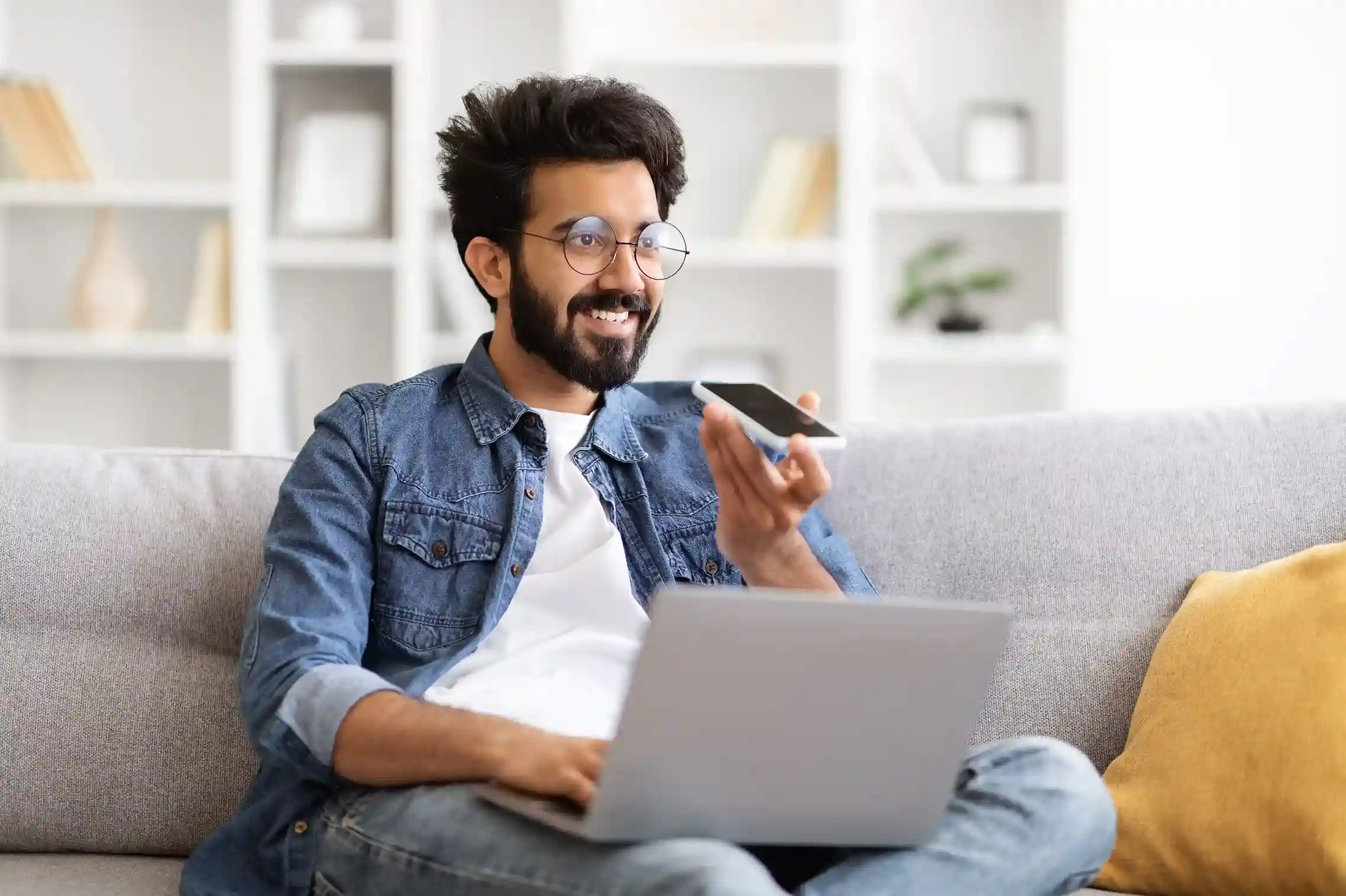 A team member calmly records a voicemail from his workspace, showing how voicemail drop supports efficient outreach without requiring live call connections. A professional records a message on his phone while reviewing work on his laptop, illustrating how voicemail drop lets agents deliver messages without interrupting recipients.