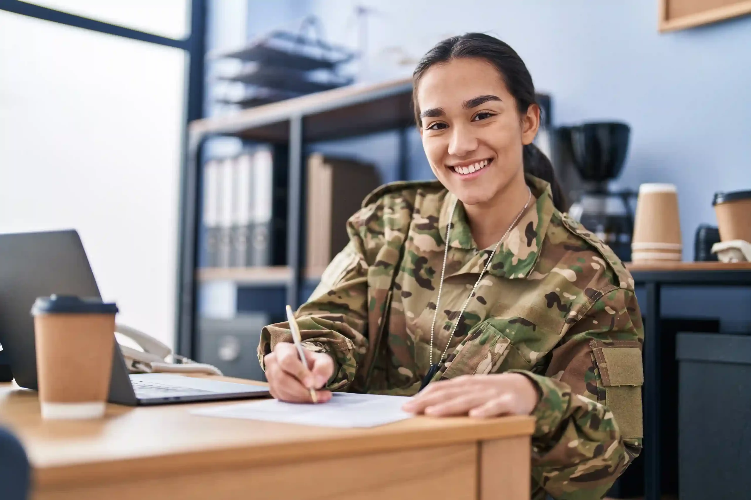 Soldier contacting his unit via Indosoft’s AI-powered military platform designed for real-time, encrypted communication. Military professional in camouflage attire working on official documents beside a laptop in a secure office environment.