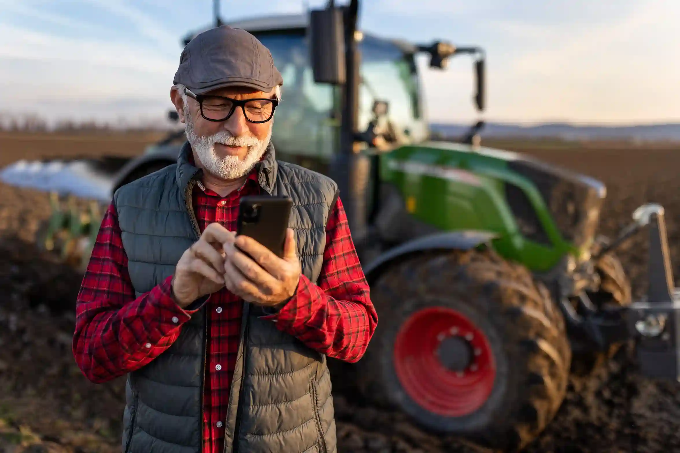 While checking his phone in the field, a farmer receives an SMS tailored to his crop growth stage, sent through a segmented contact group. A farmer stands among growing crops, reading a targeted SMS update on his phone that provides timely guidance based on his current crop conditions.