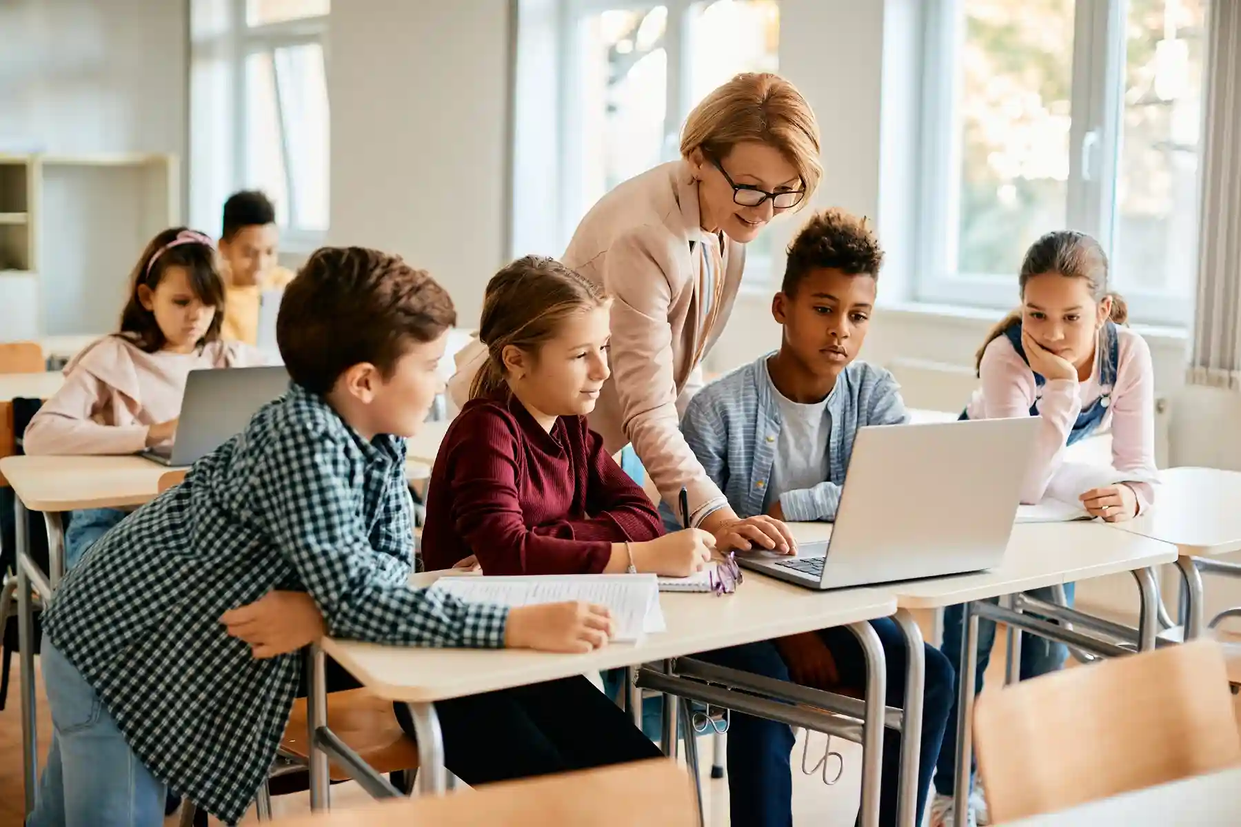A teacher works closely with students as they review enrollment requirements on a laptop, demonstrating how Indosoft provides step-by-step digital guidance and reminders. Teacher assisting a group of students on a laptop as they review enrollment steps using Indosoft’s guided digital tools.
